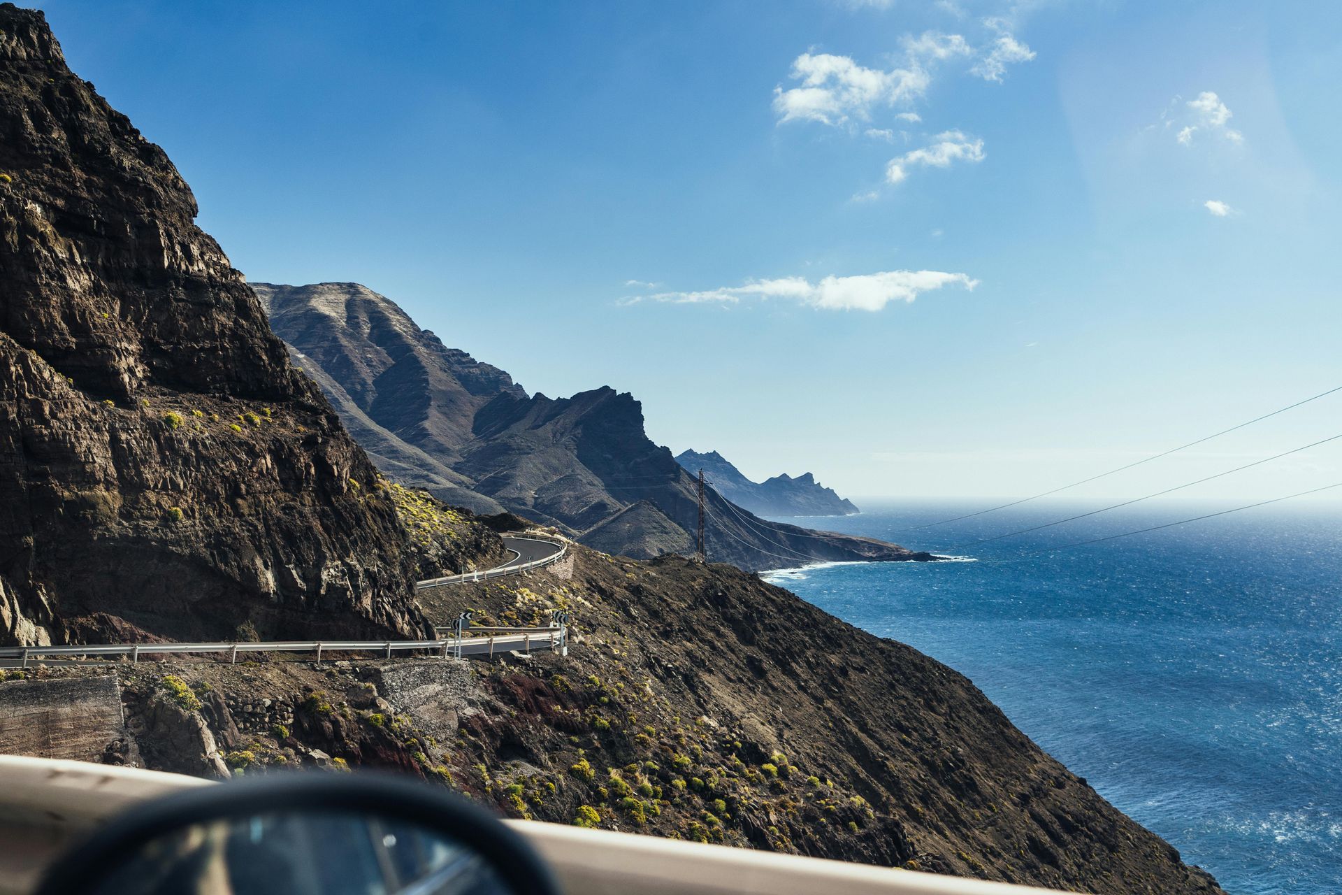 A car is driving down a mountain road next to the ocean.
