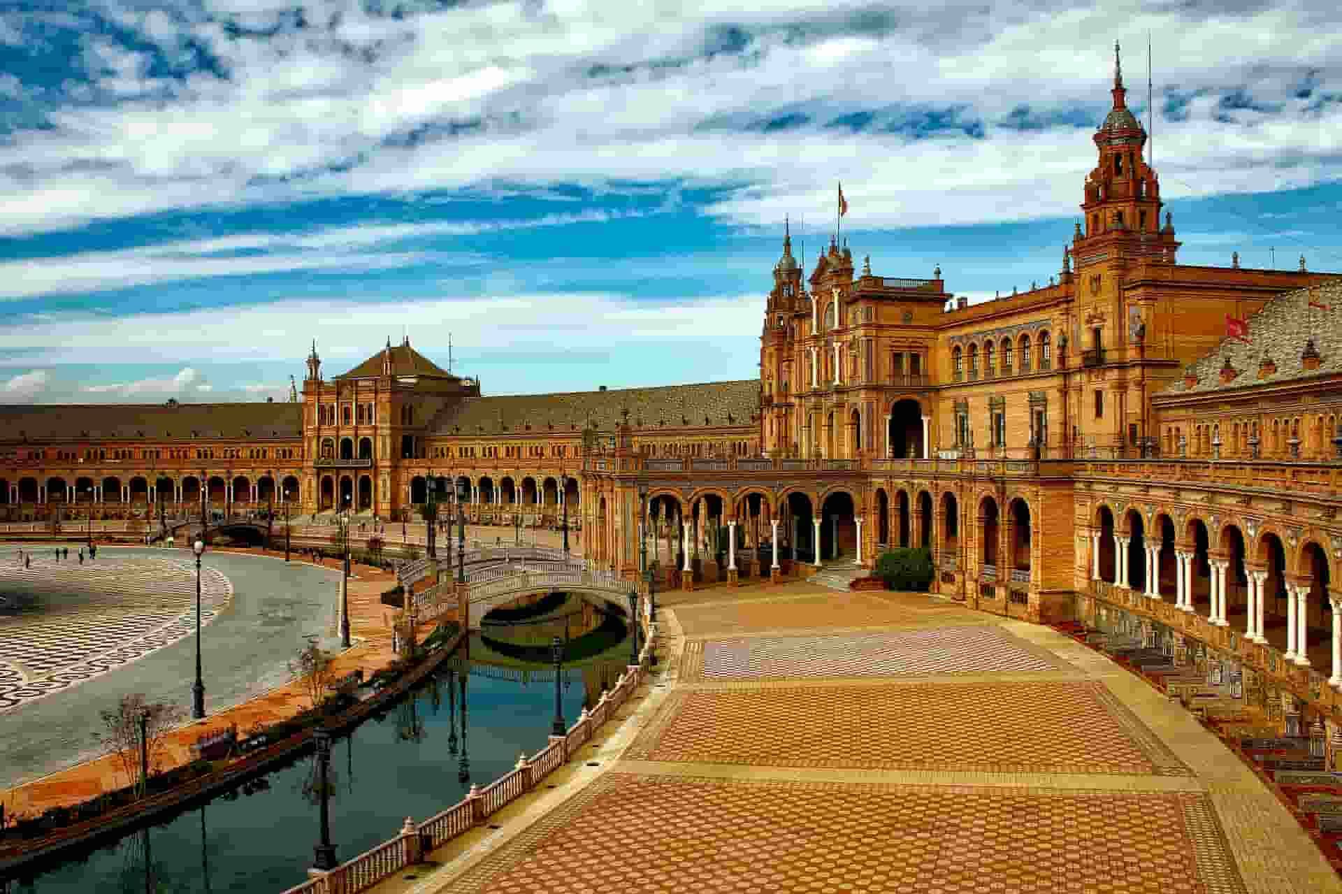 A man in a boat is rowing down a river in front of a large building in Seville
