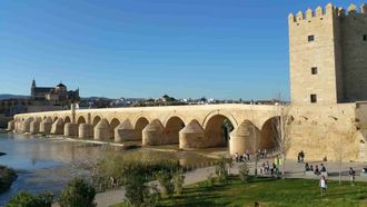 A bridge over a river in Cordoba with a church in the background