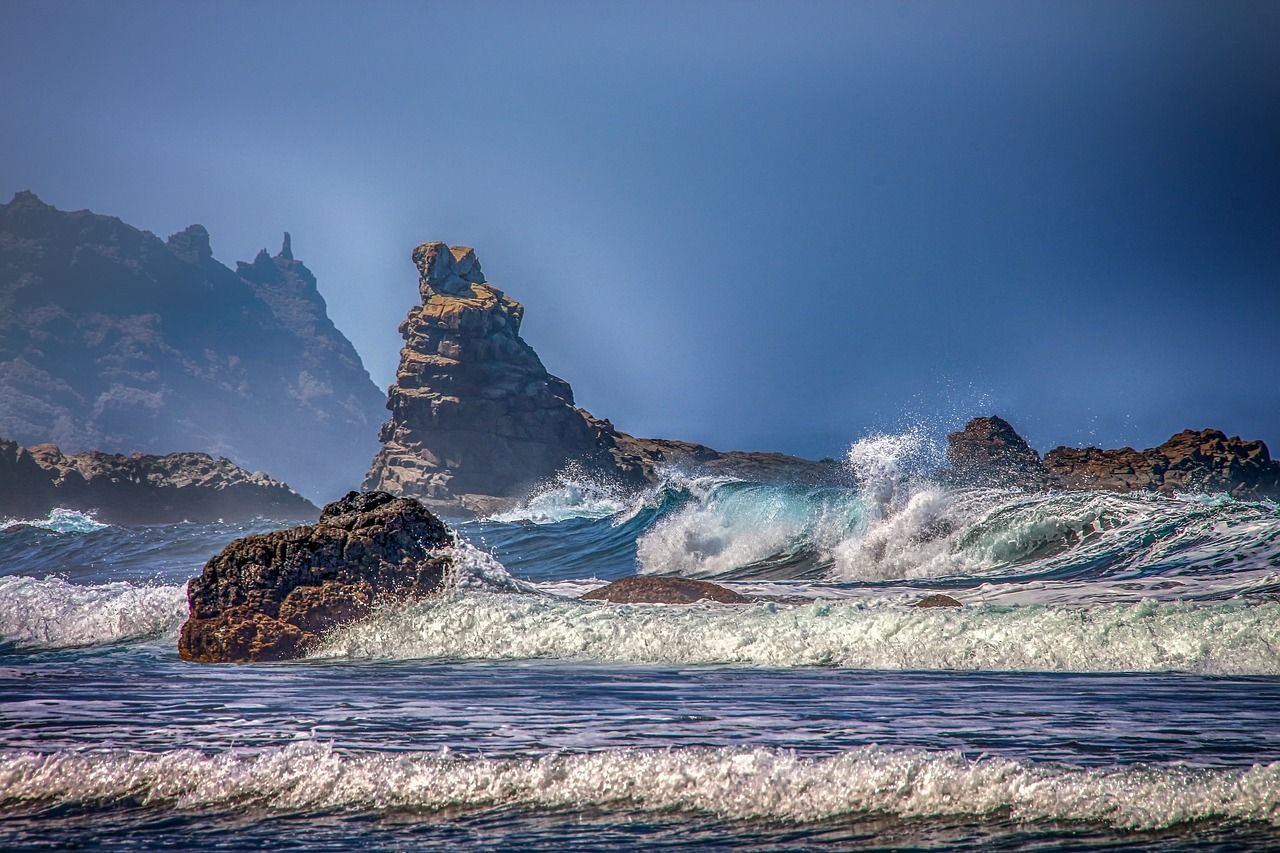 A large rock formation in the middle of the ocean with waves crashing against it.