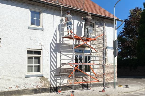Two men are painting the side of a building on a scaffolding.