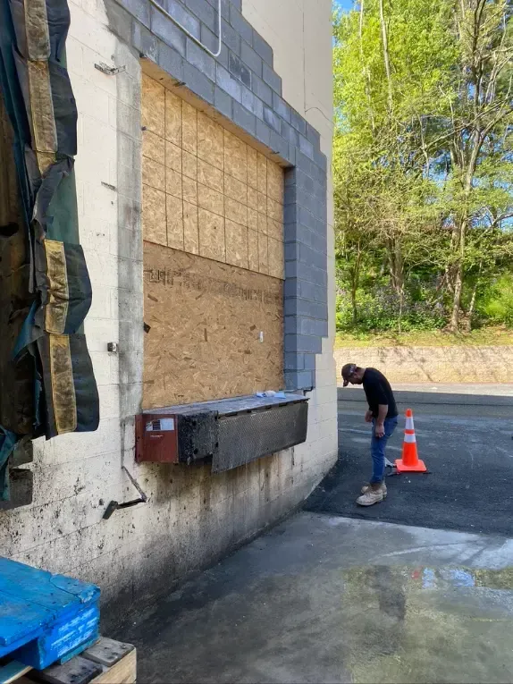 A man is standing in front of a building with a window boarded up.