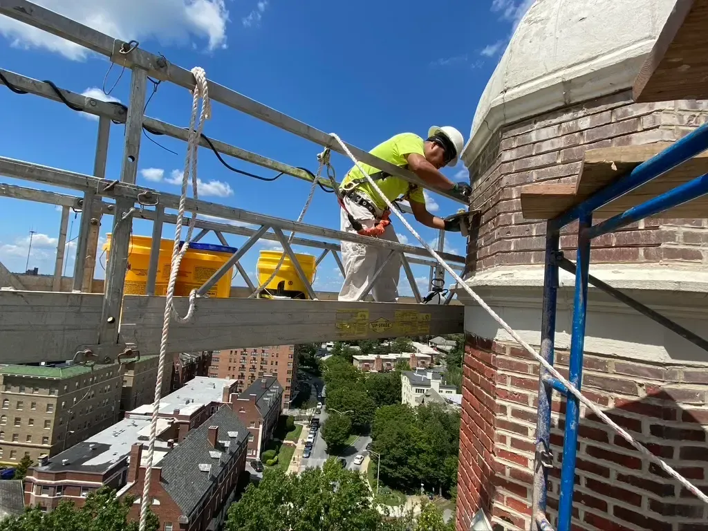 A man is working on a brick building on a scaffolding.