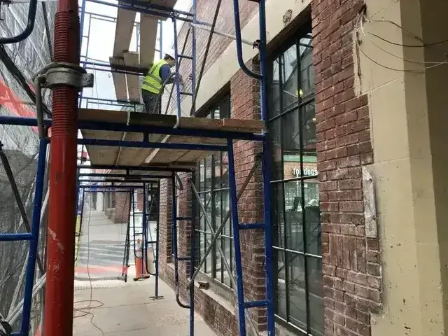 Construction worker on scaffolding repairing brick building exterior.