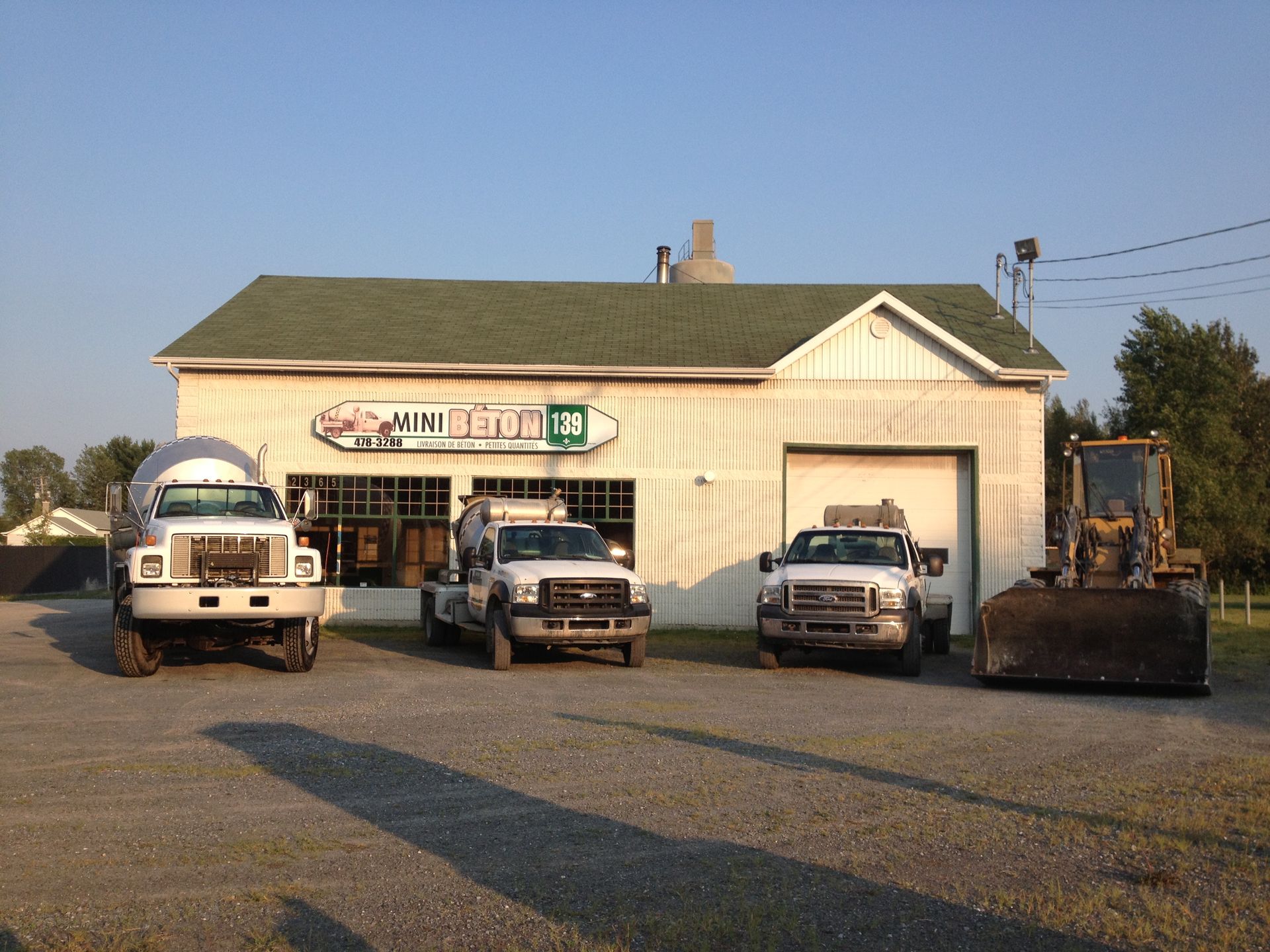 Trois camions sont garés devant un bâtiment avec un toit vert