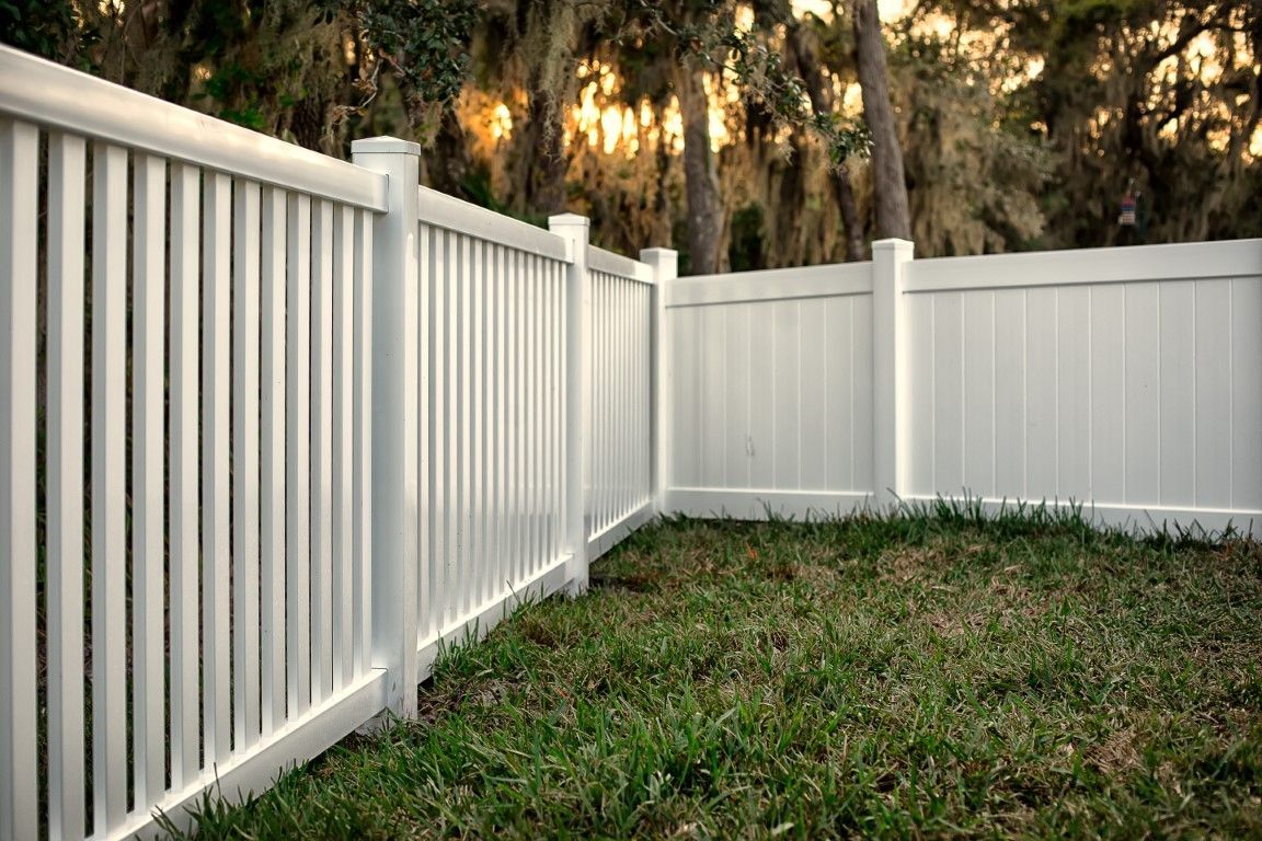 White vinyl fence enclosing a grassy yard with trees in the background.