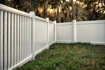 White vinyl fence enclosing a grassy yard with trees in the background.