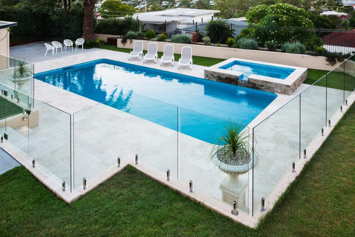 Swimming pool and spa with glass fence, white chairs, and green lawn.