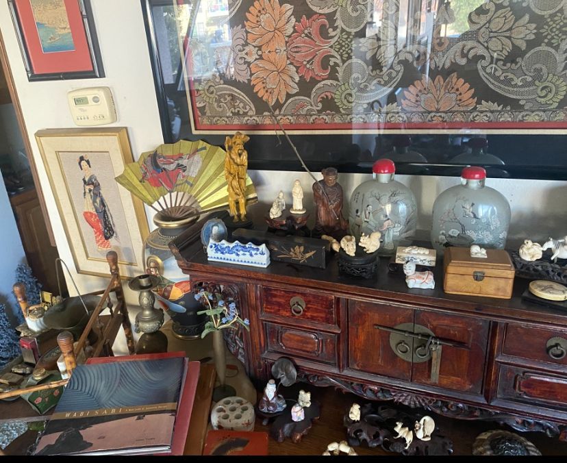 A collection of Asian-inspired antiques on a wooden cabinet, including art, vases, and small figurines.