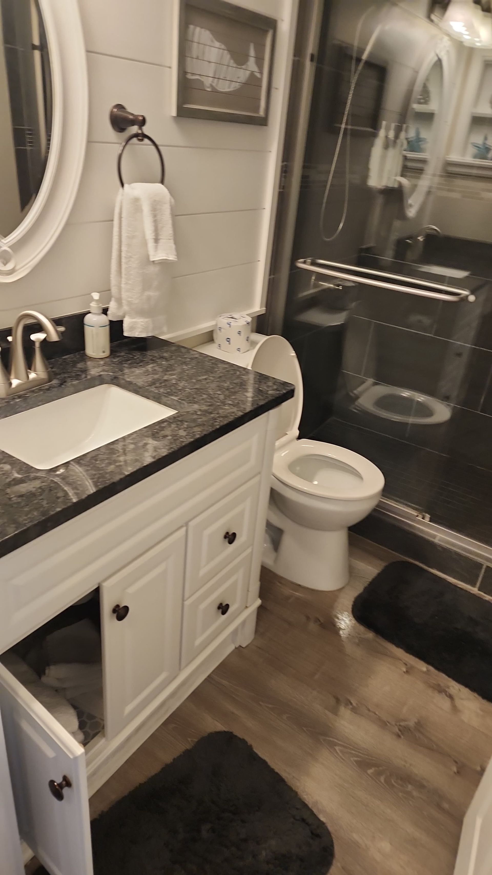 Bathroom with white vanity, dark countertop, toilet, and shower. Black rug on floor.