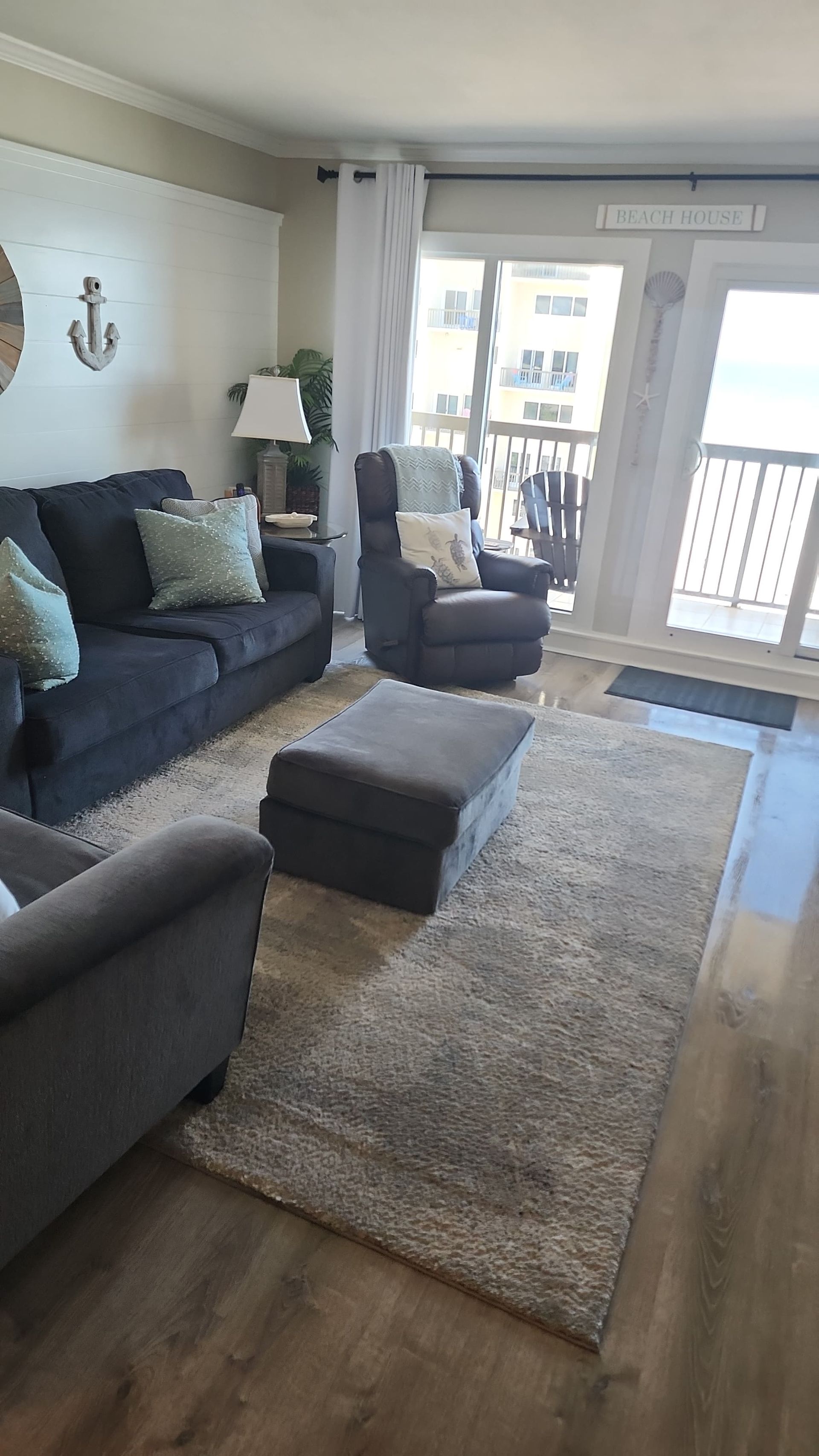 Living room with gray sofa, ottoman, and armchair; rug, sliding glass doors to balcony.