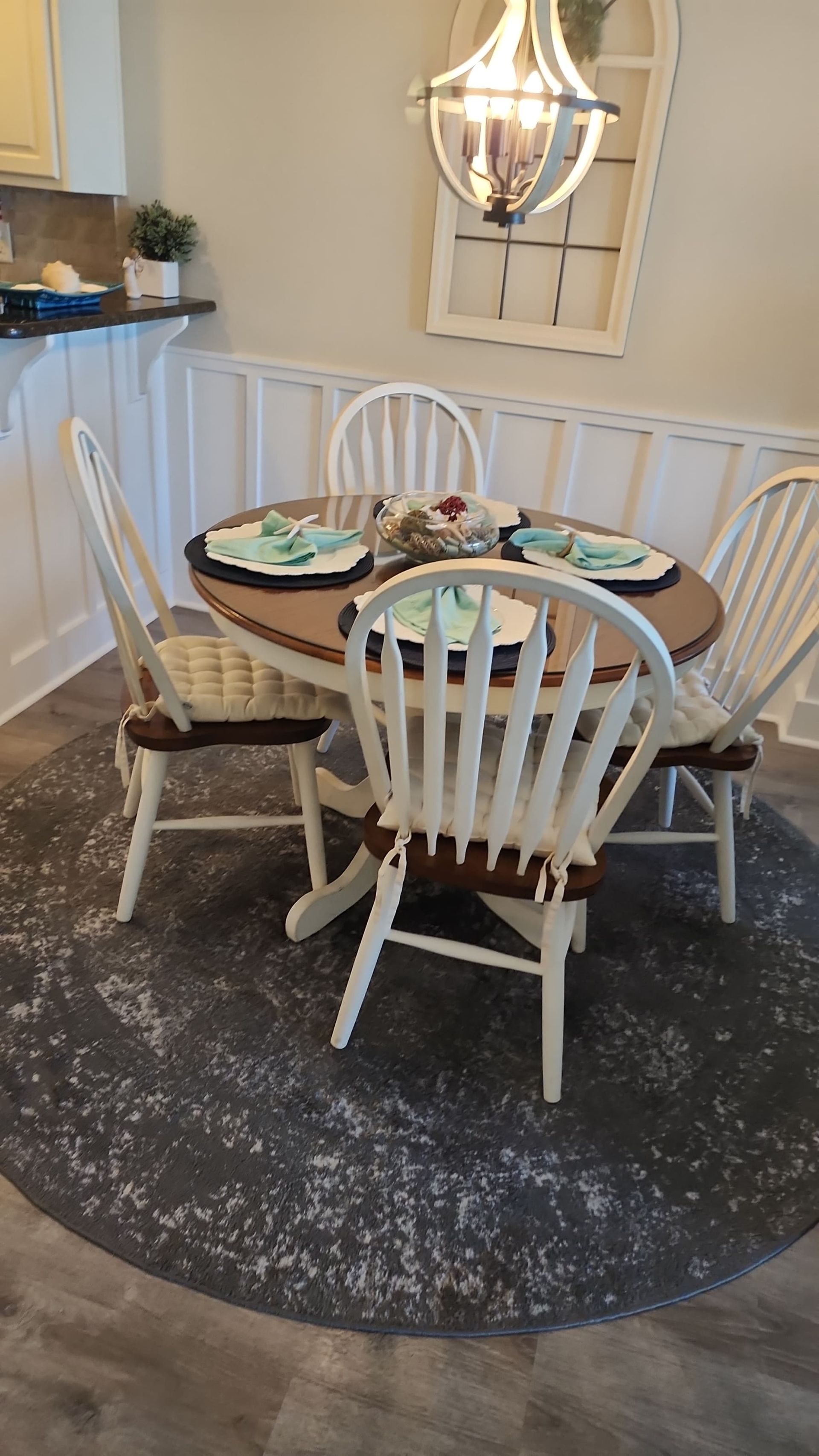 Round dining table set for four, white chairs with brown seats, atop gray rug.