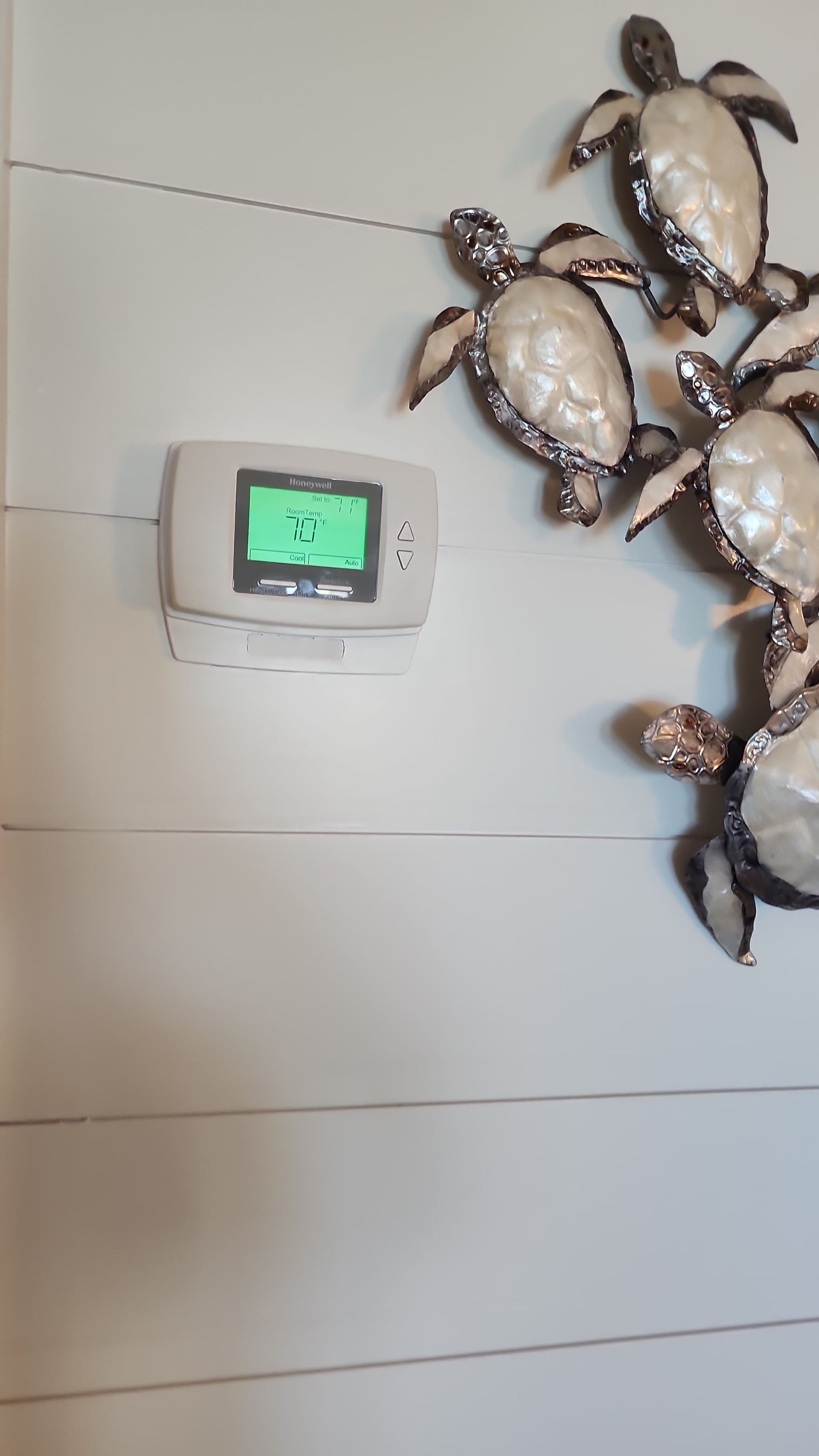 Thermostat on a white paneled wall with decorative turtle art.
