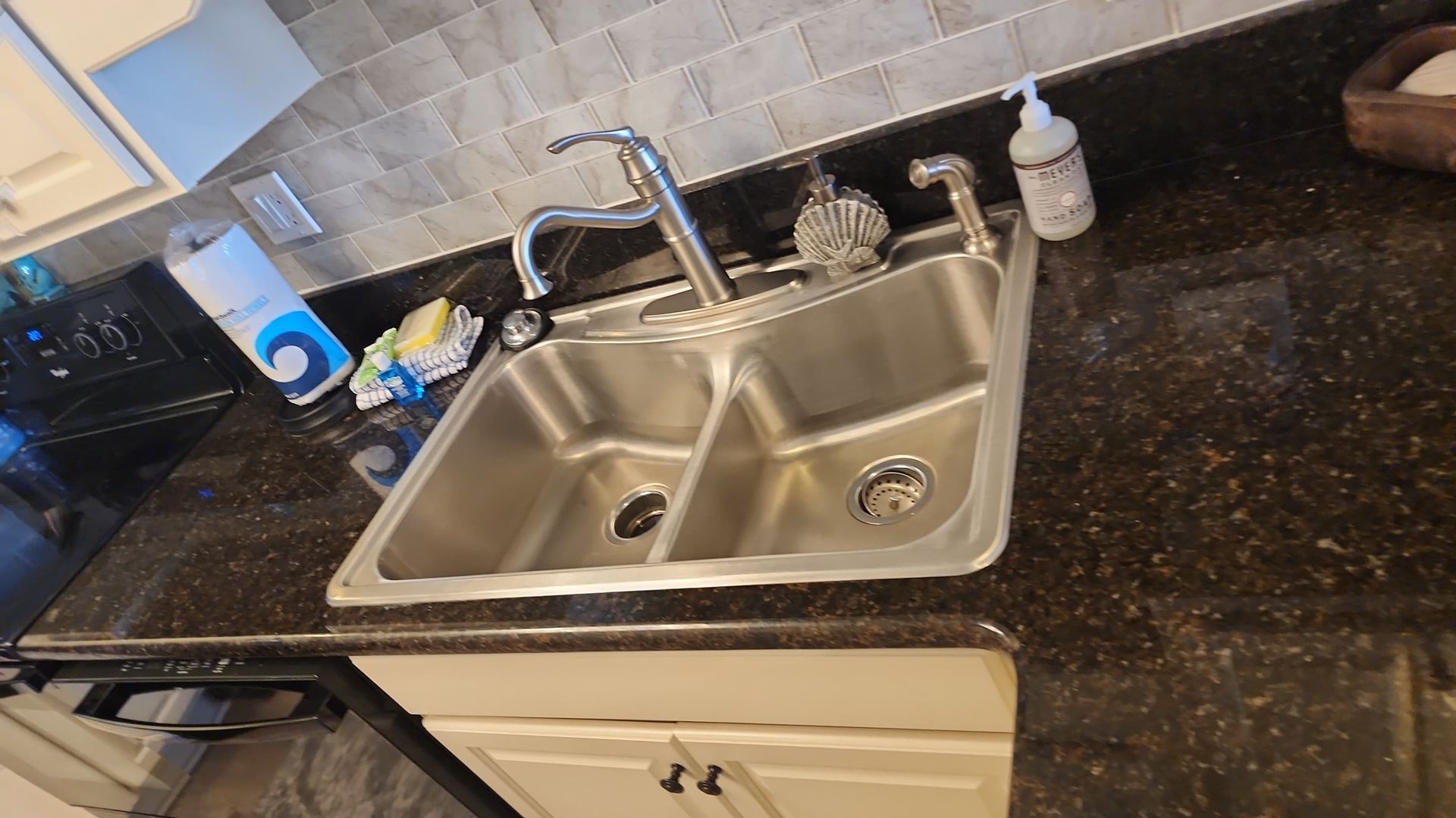 Stainless steel kitchen sink in a dark countertop with a faucet and soap dispenser.