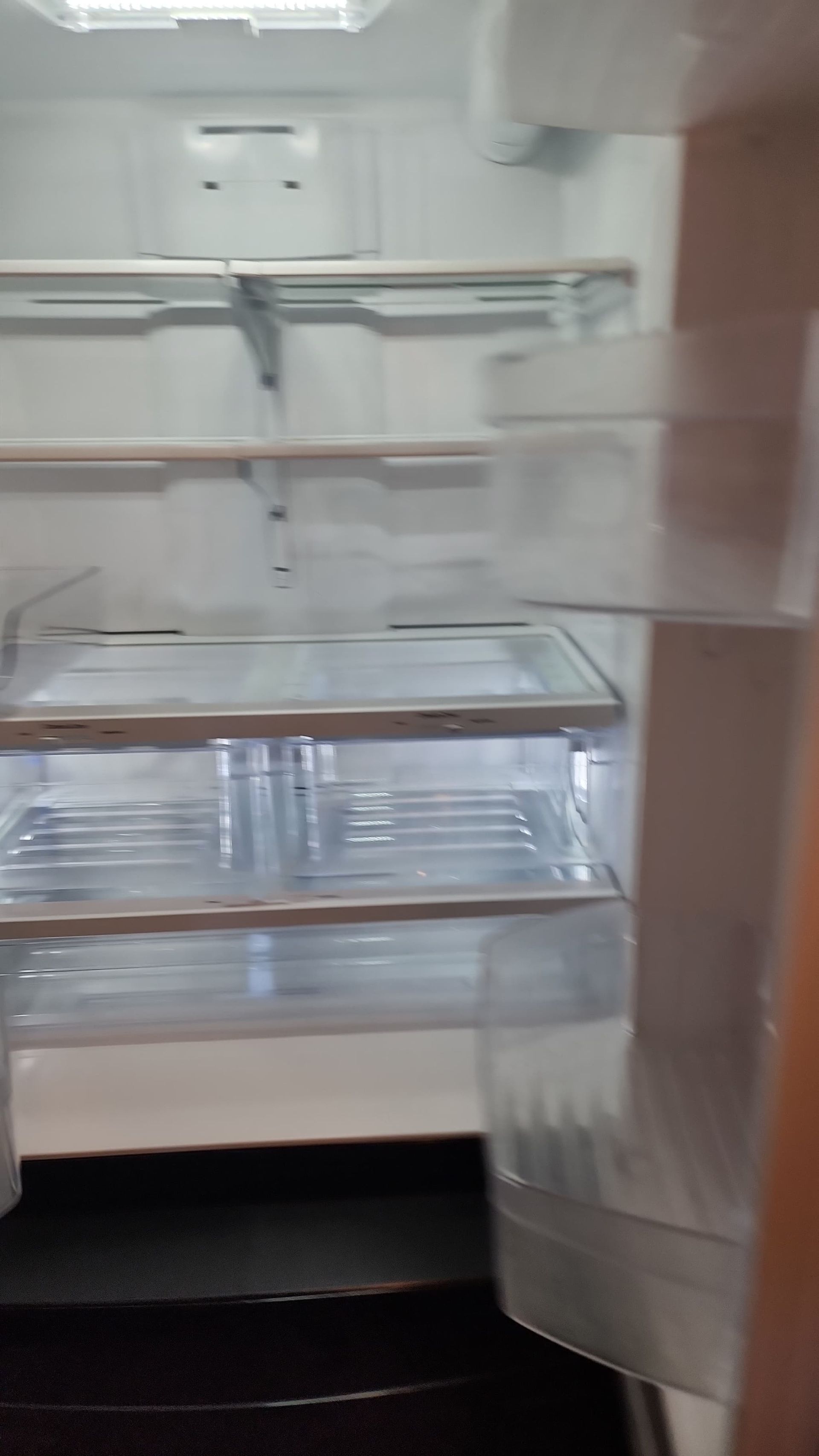 Empty refrigerator interior, shelves visible. Lit by overhead light. Door open.