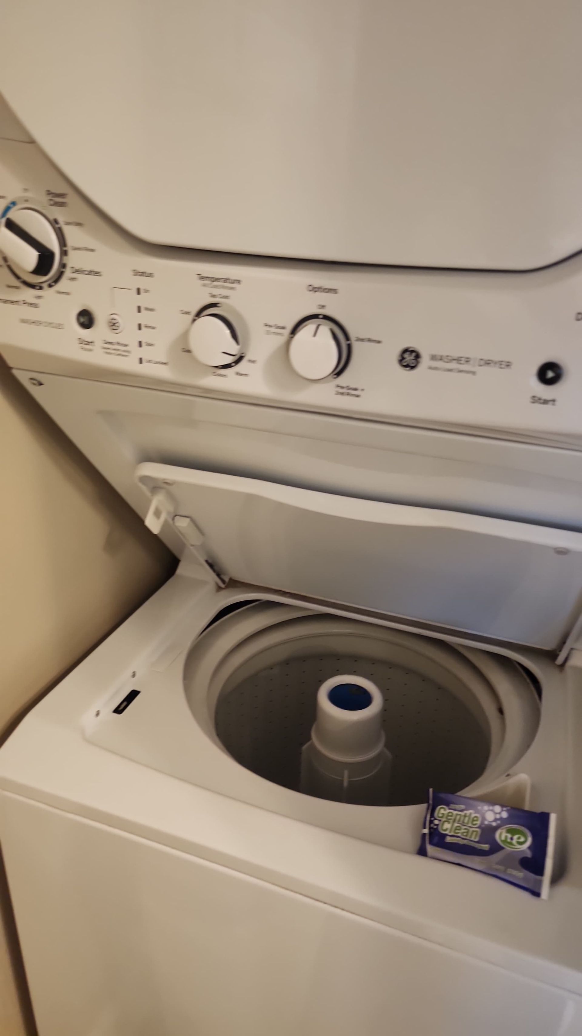White stacked GE washer and dryer unit, with the washing machine lid open and a detergent box on top.