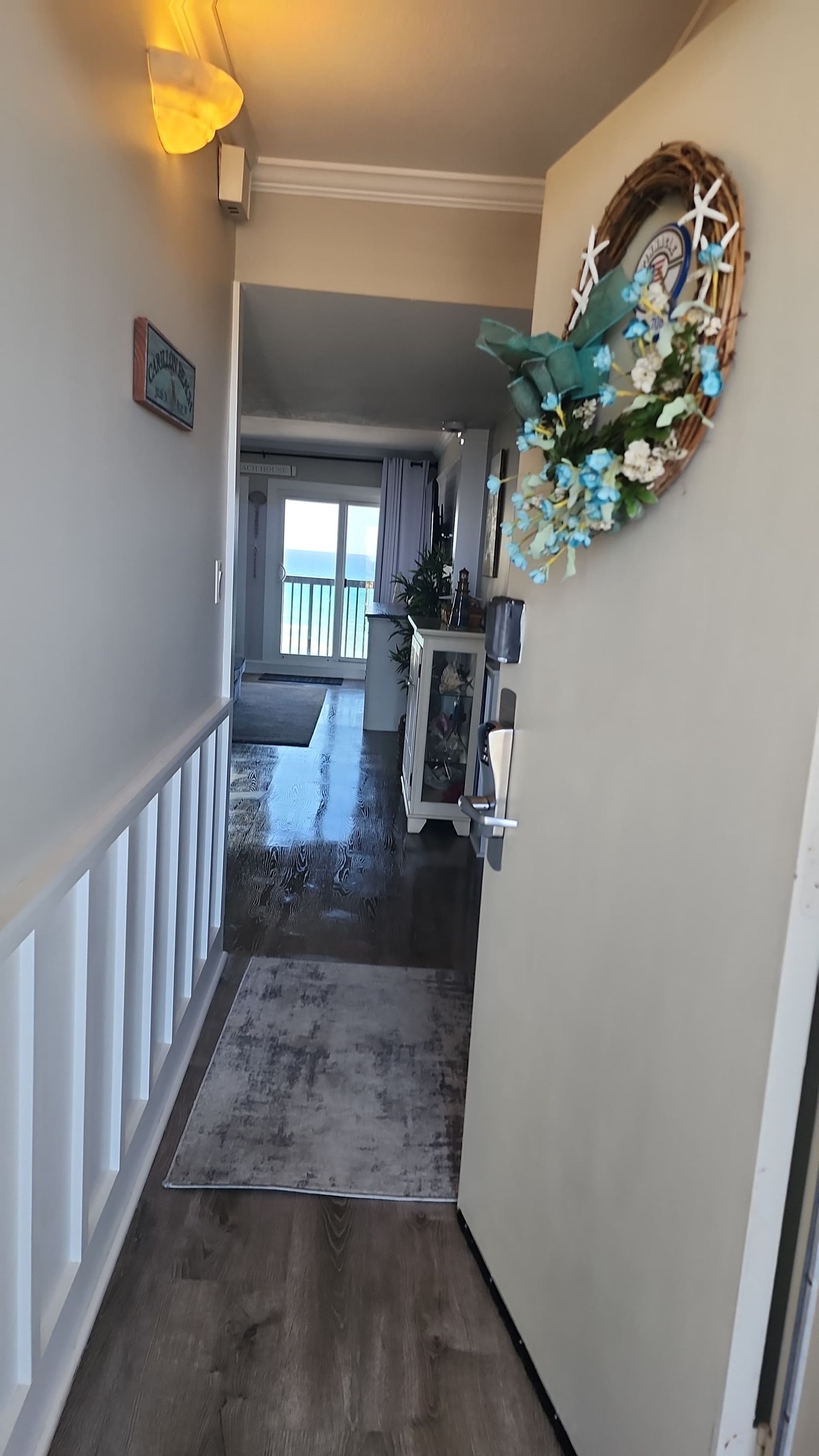 Hallway with rug, open door, and ocean view in the distance. Coastal decor on wall.