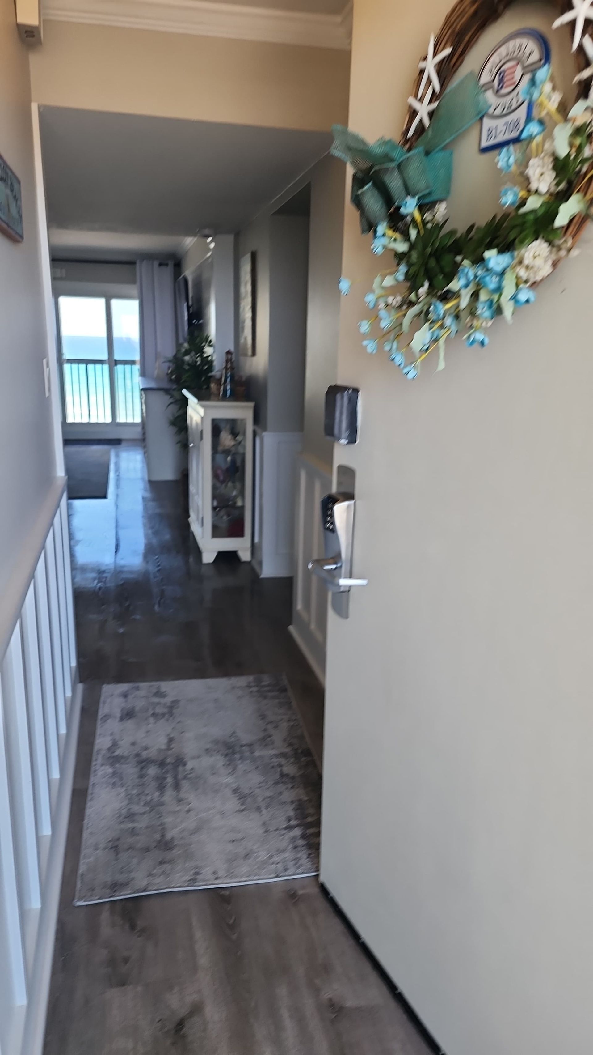 Entryway: open door with wreath, rug, hallway leading to window with ocean view.
