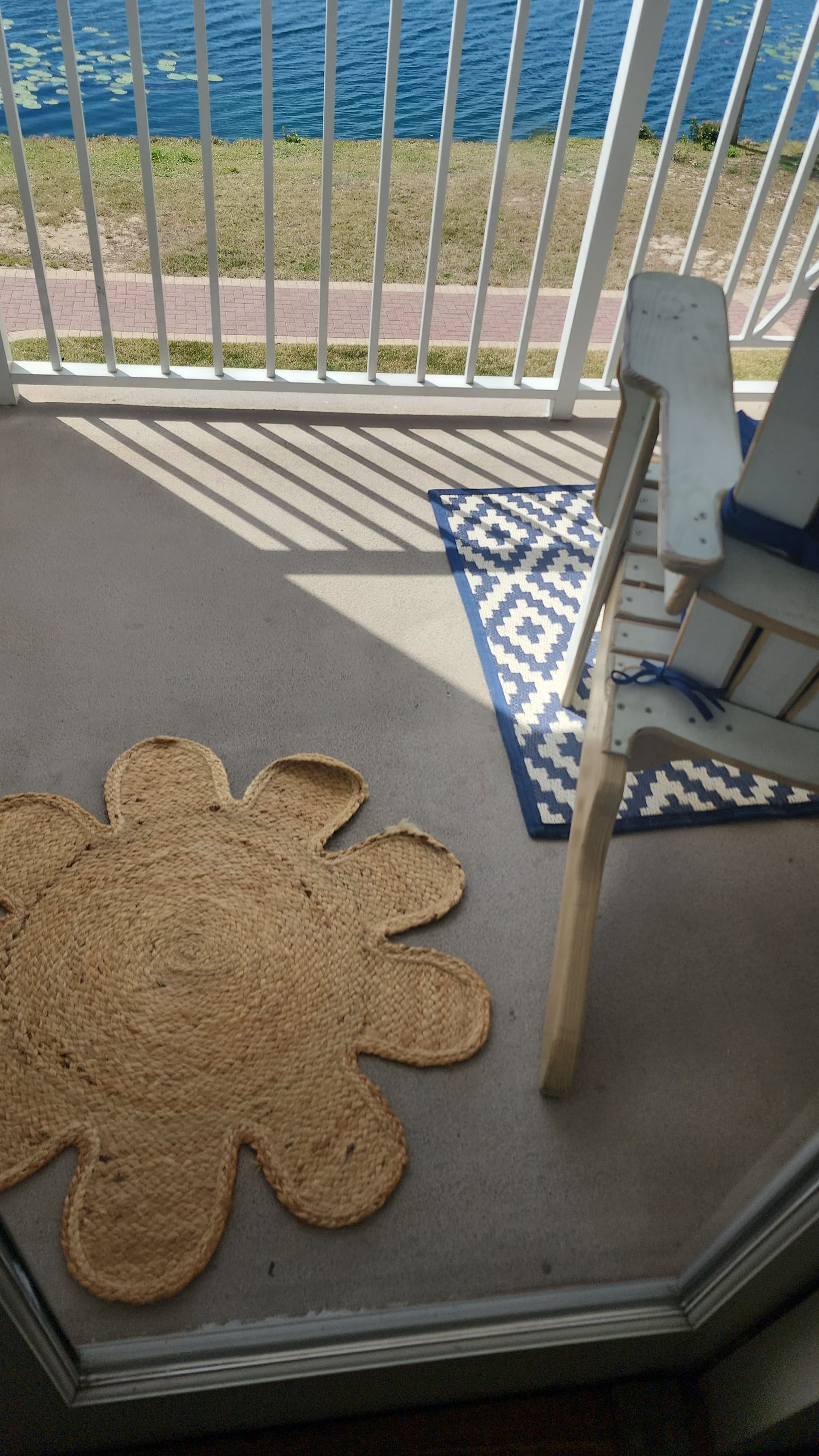 A daisy-shaped rug on a porch with a blue and white patterned rug and a white chair, overlooking water.