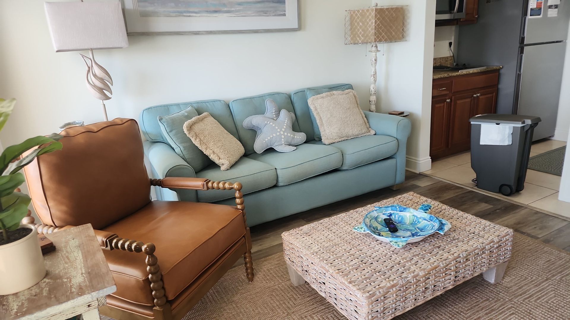 Living room with blue sofa, brown armchair, woven coffee table, and lamps.