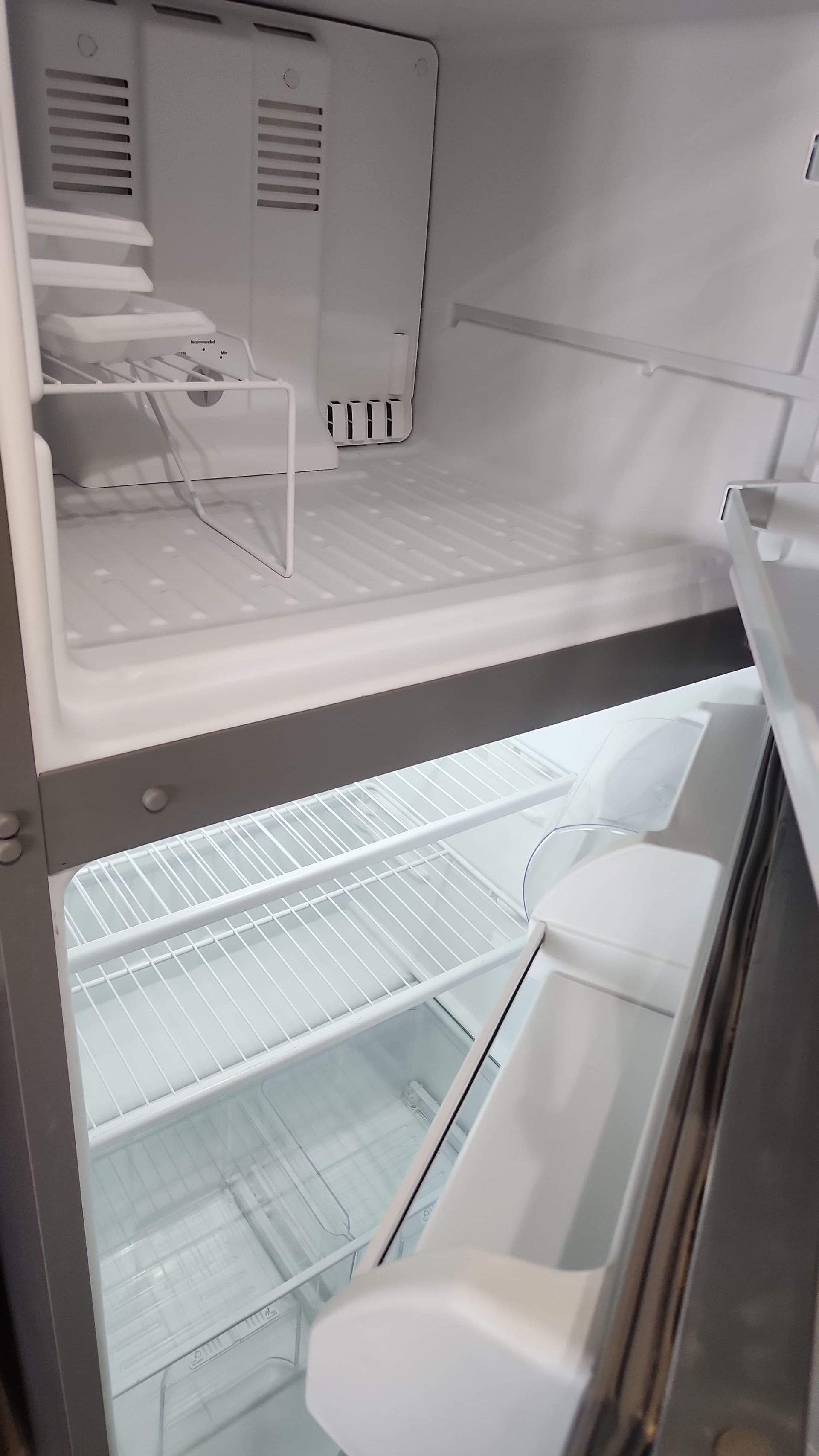 Empty, open refrigerator with shelves and door storage. Interior is white and gray.