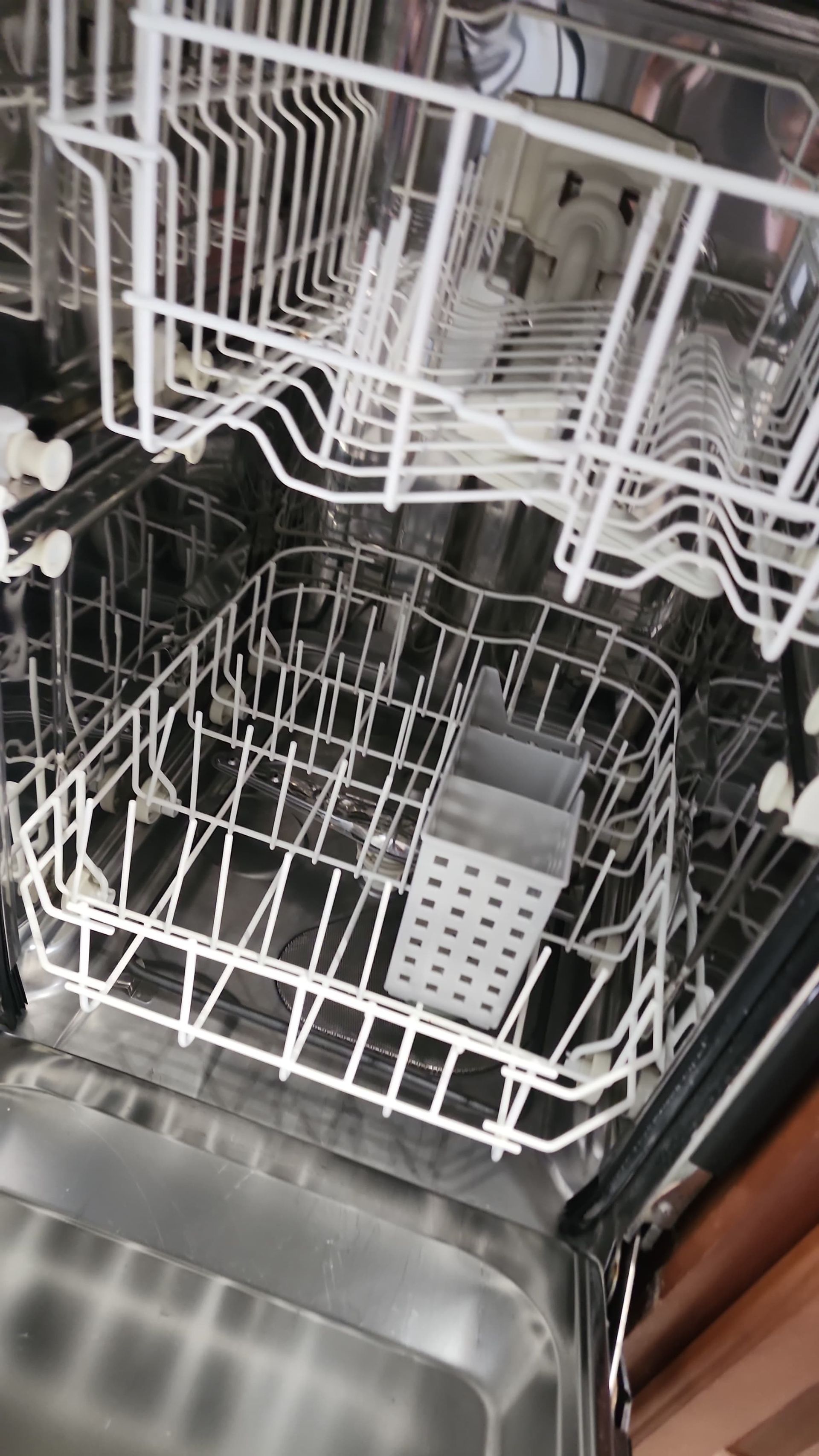 Open dishwasher with empty racks, including a silverware basket.