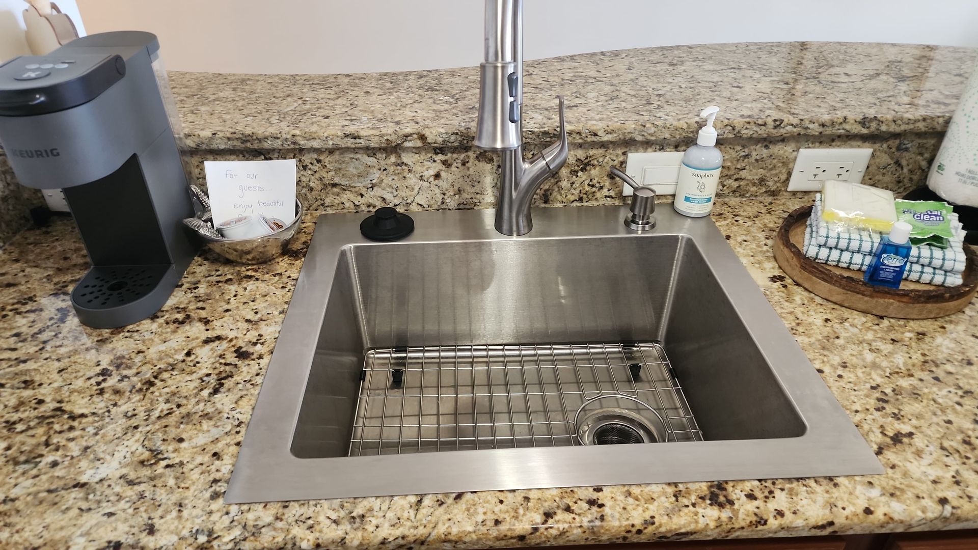 Stainless steel kitchen sink with faucet, Keurig, and dish soap on granite countertop.