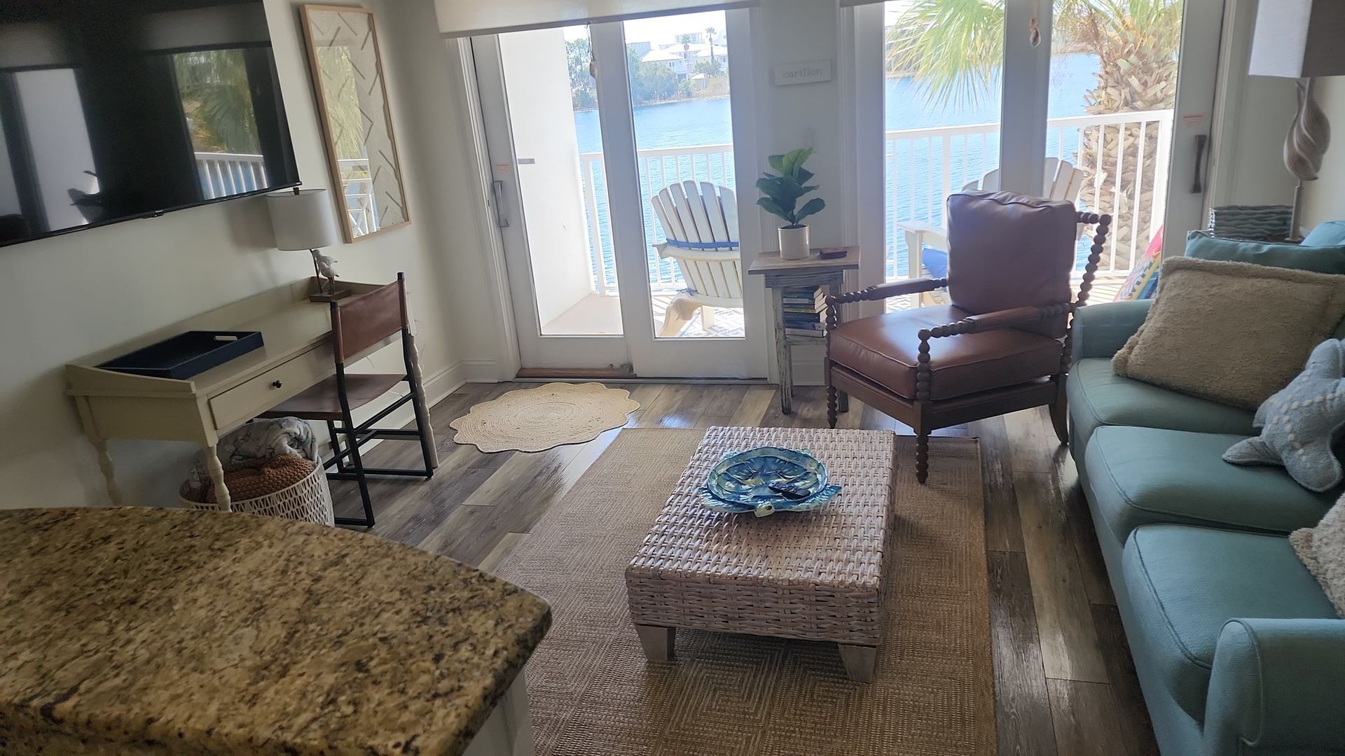 Living room with view of water; blue sofa, brown chair, desk, and sliding glass doors.