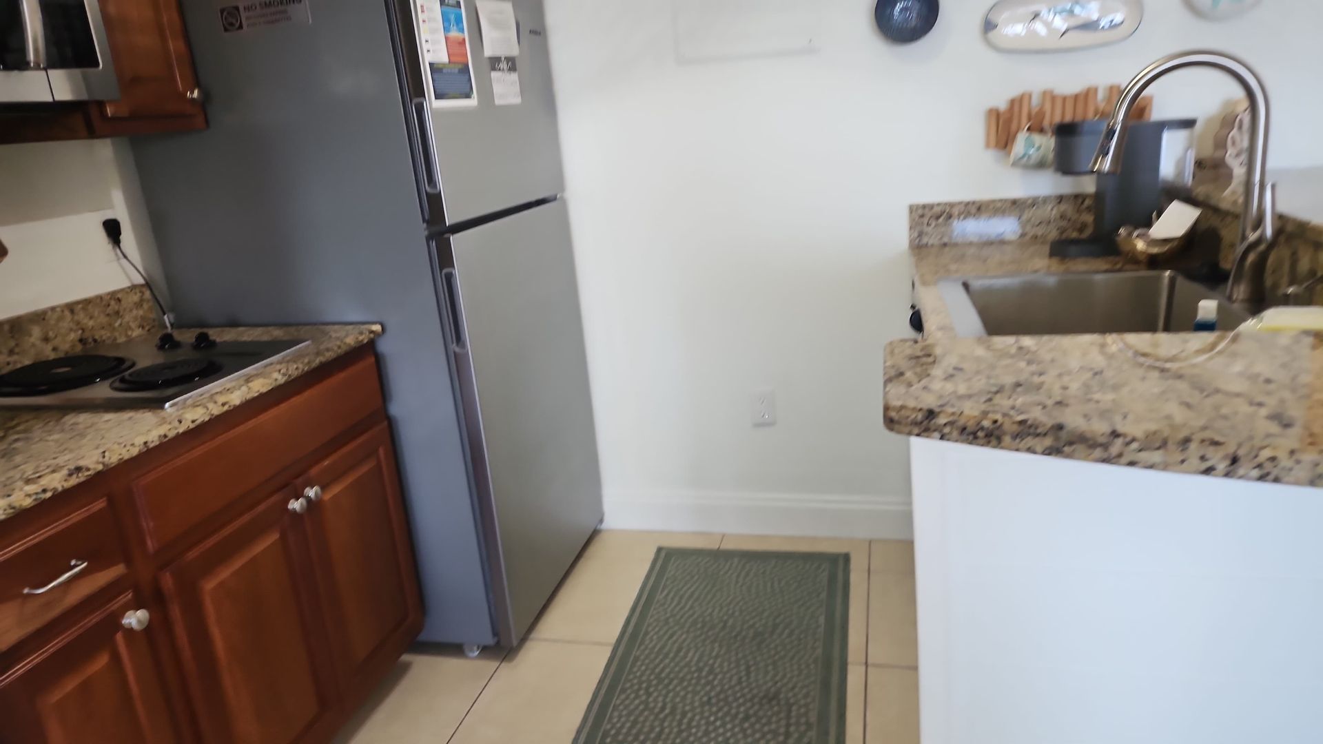 Kitchen with stainless steel refrigerator, dark wood cabinets, granite countertops, and a gray rug.