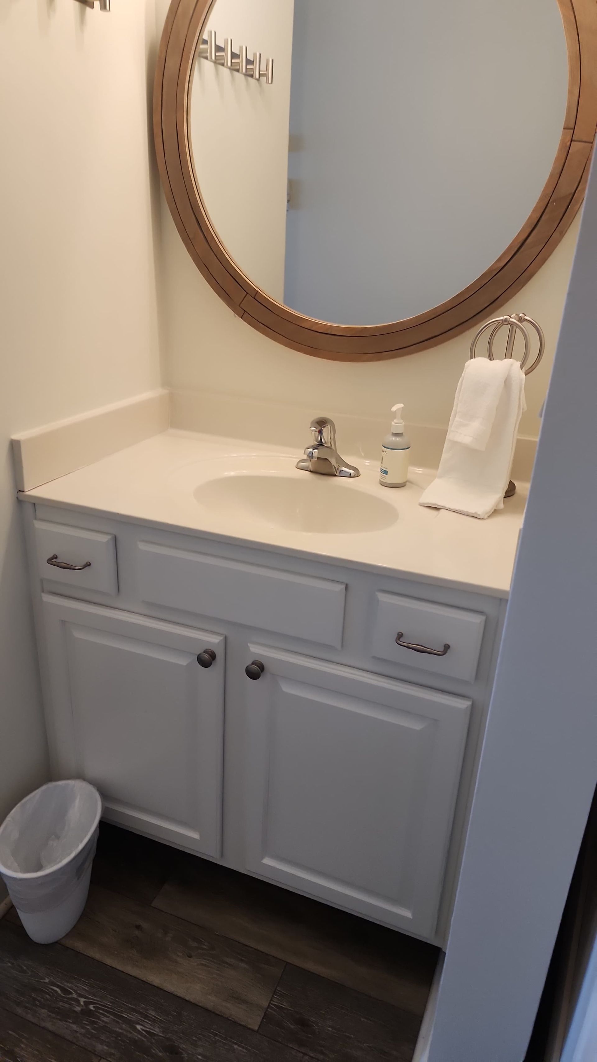 White bathroom vanity with oval mirror, sink, and towel rack. Trash can in the corner.
