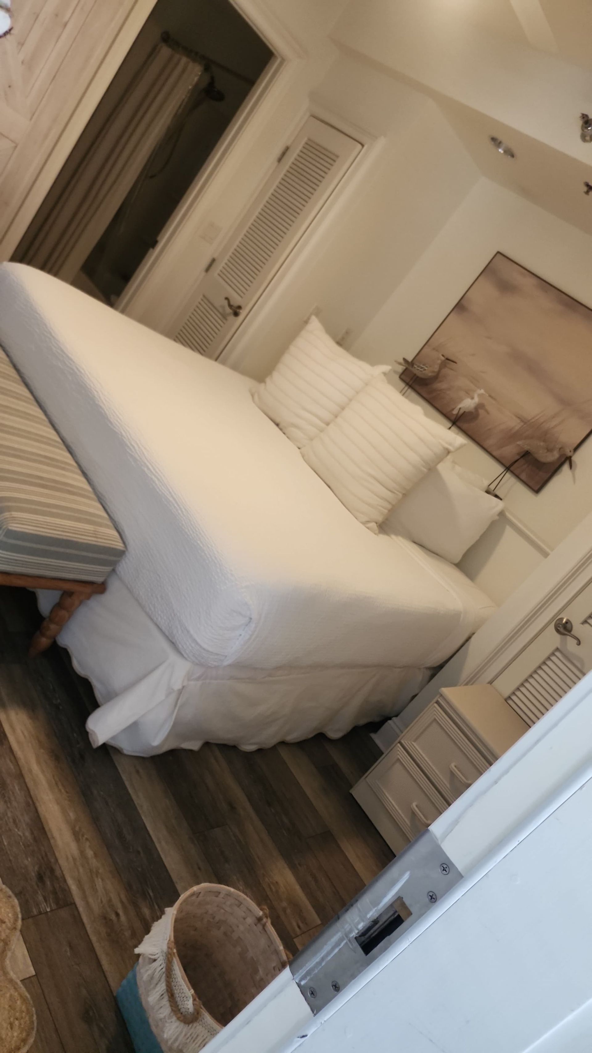 Bedroom with white bedding, wood-look floor, and beige artwork.