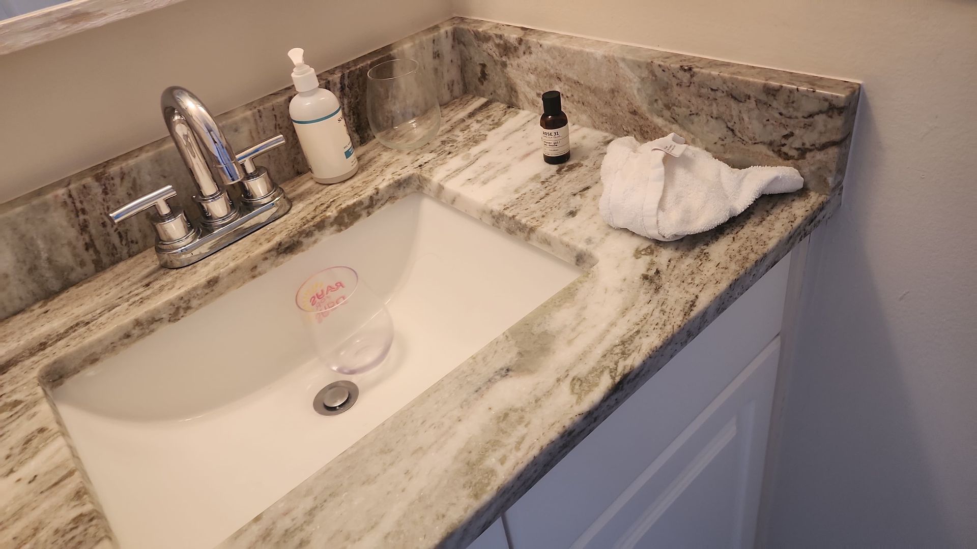 Bathroom sink with granite countertop. Soap dispenser, washcloth, and bottle on the counter.