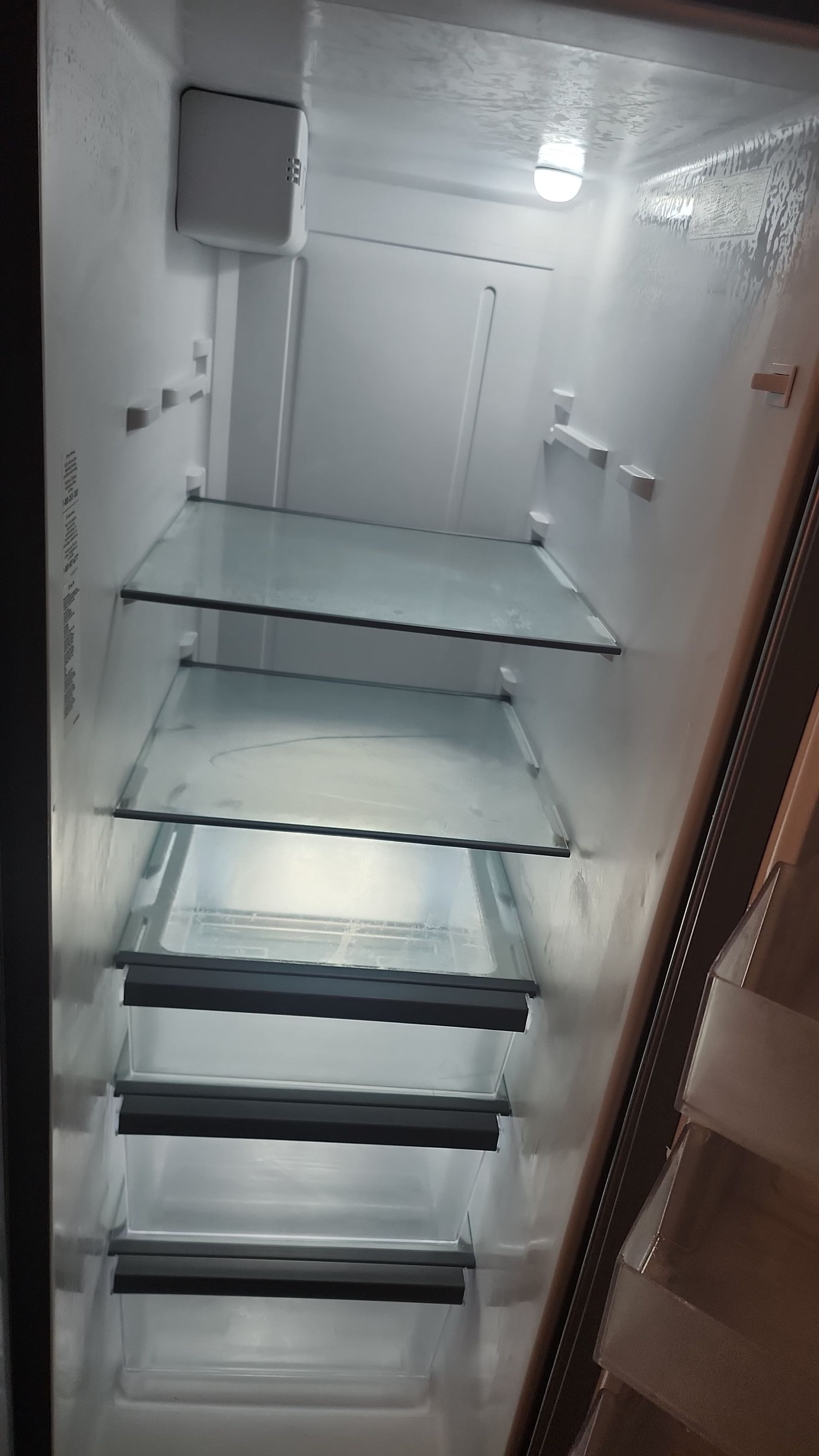 Empty, lit refrigerator interior with glass shelves.