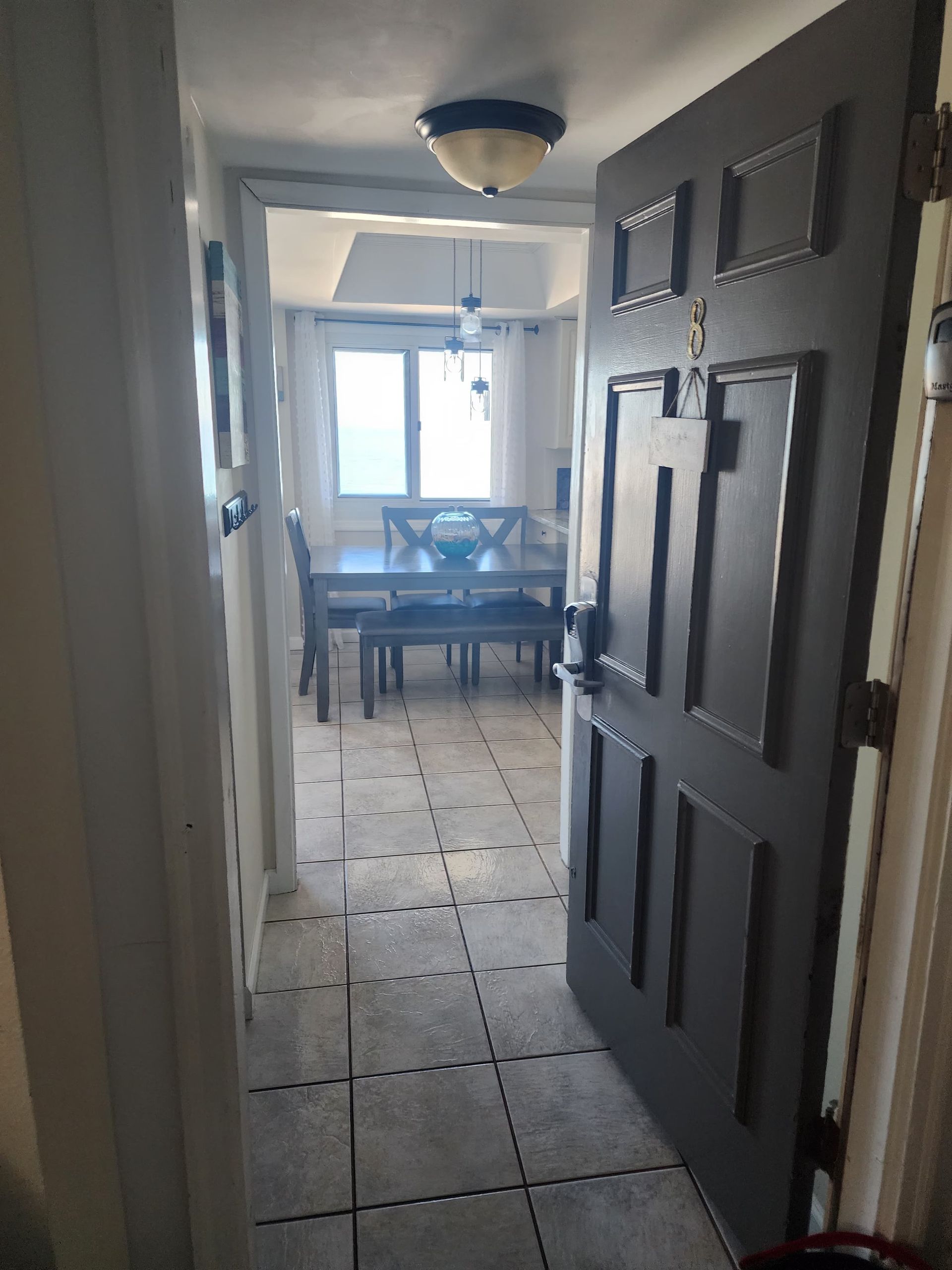 Open gray door leads to dining room with table and chairs. Tile floor.