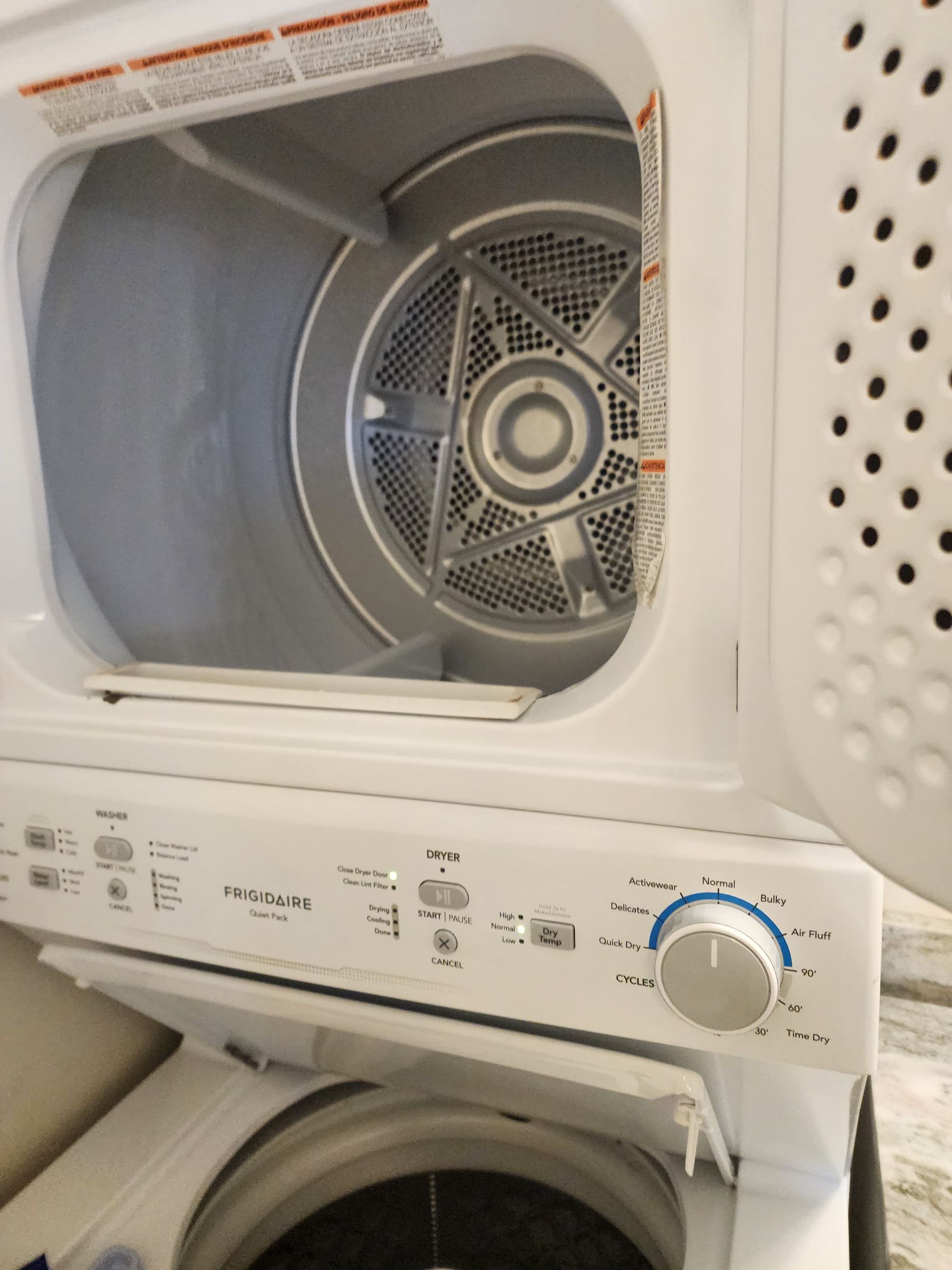White dryer with an open door, stacked above a washing machine. The dryer’s interior is visible.