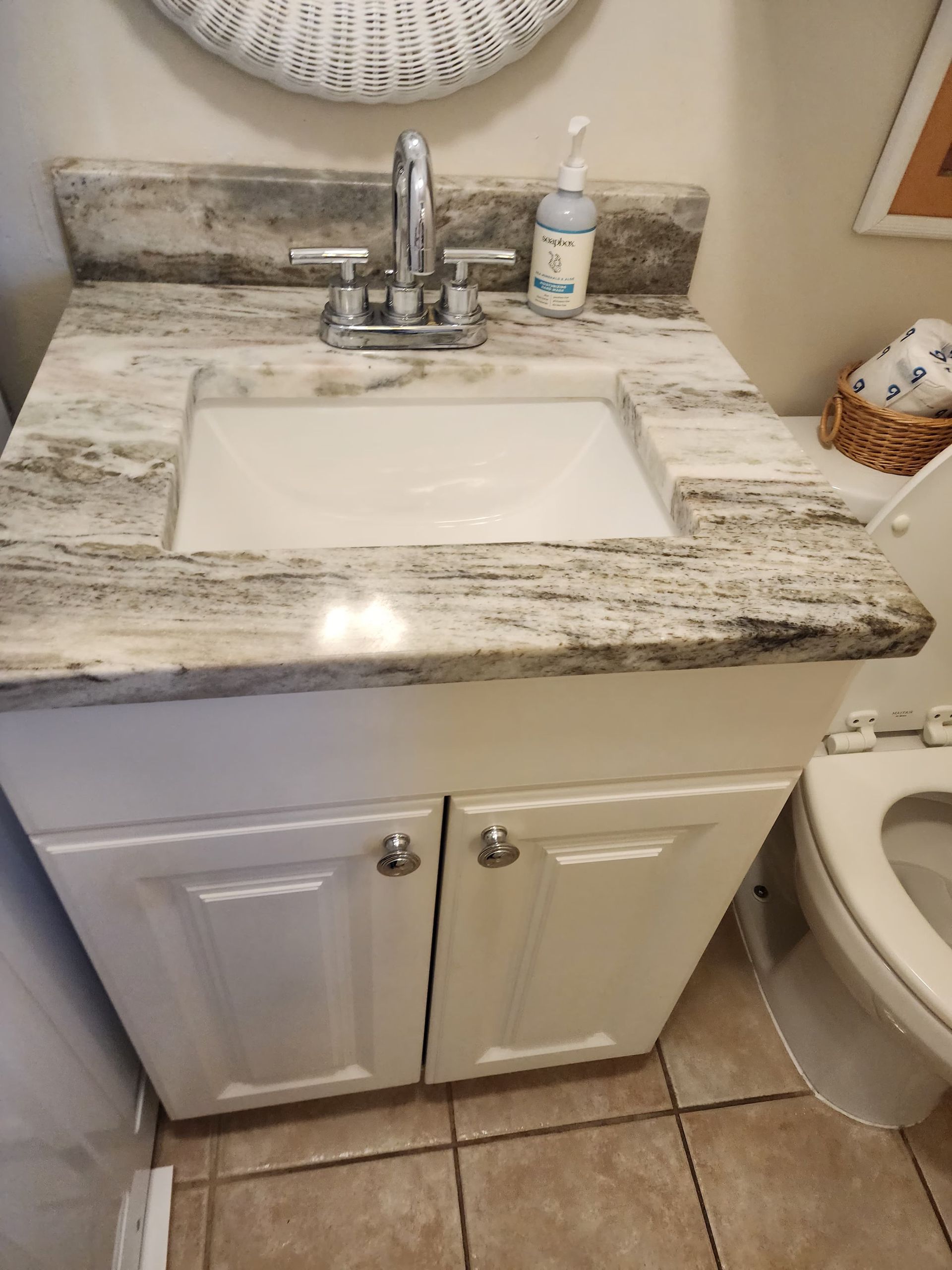 White bathroom vanity with marble countertop, silver faucet, and white sink.