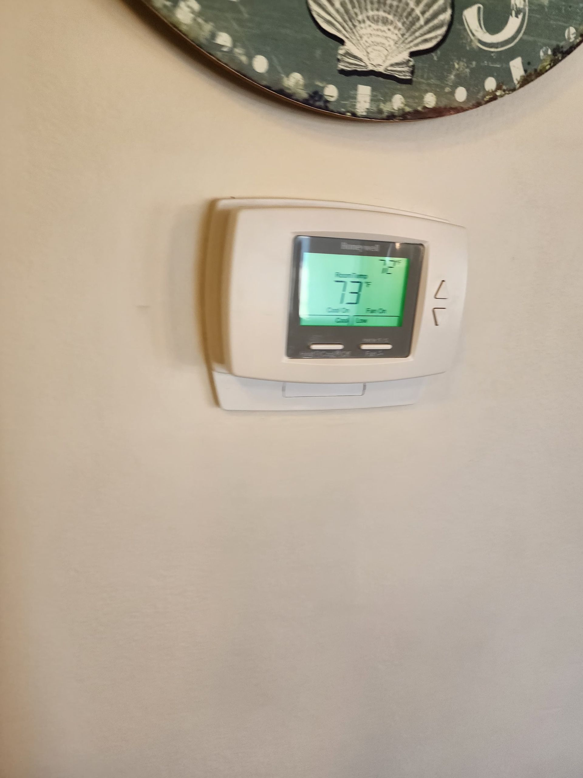 White thermostat on a wall, displaying 73 degrees. A decorative item is above it.