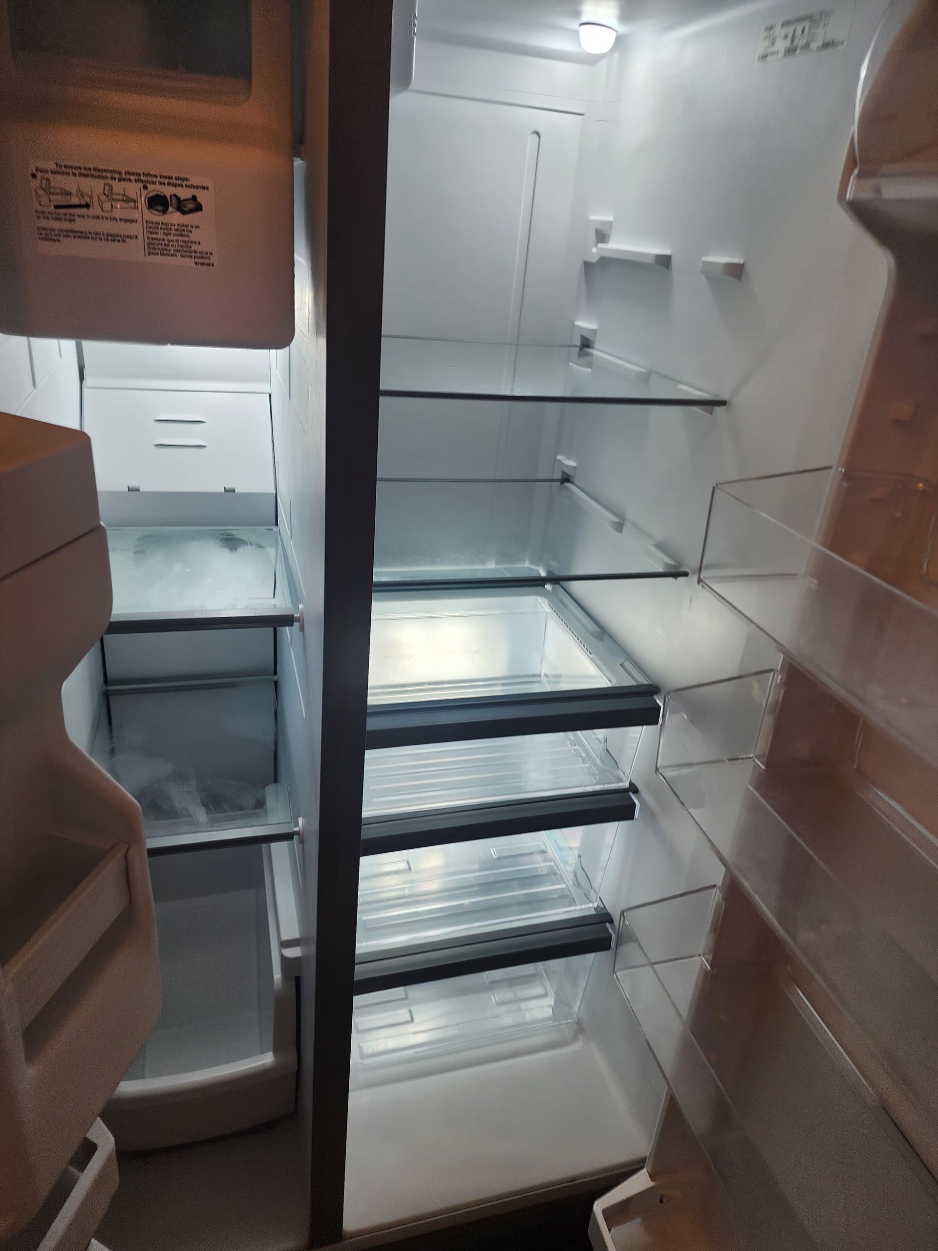 Empty, open refrigerator; shelves and drawers visible. Bright interior light.