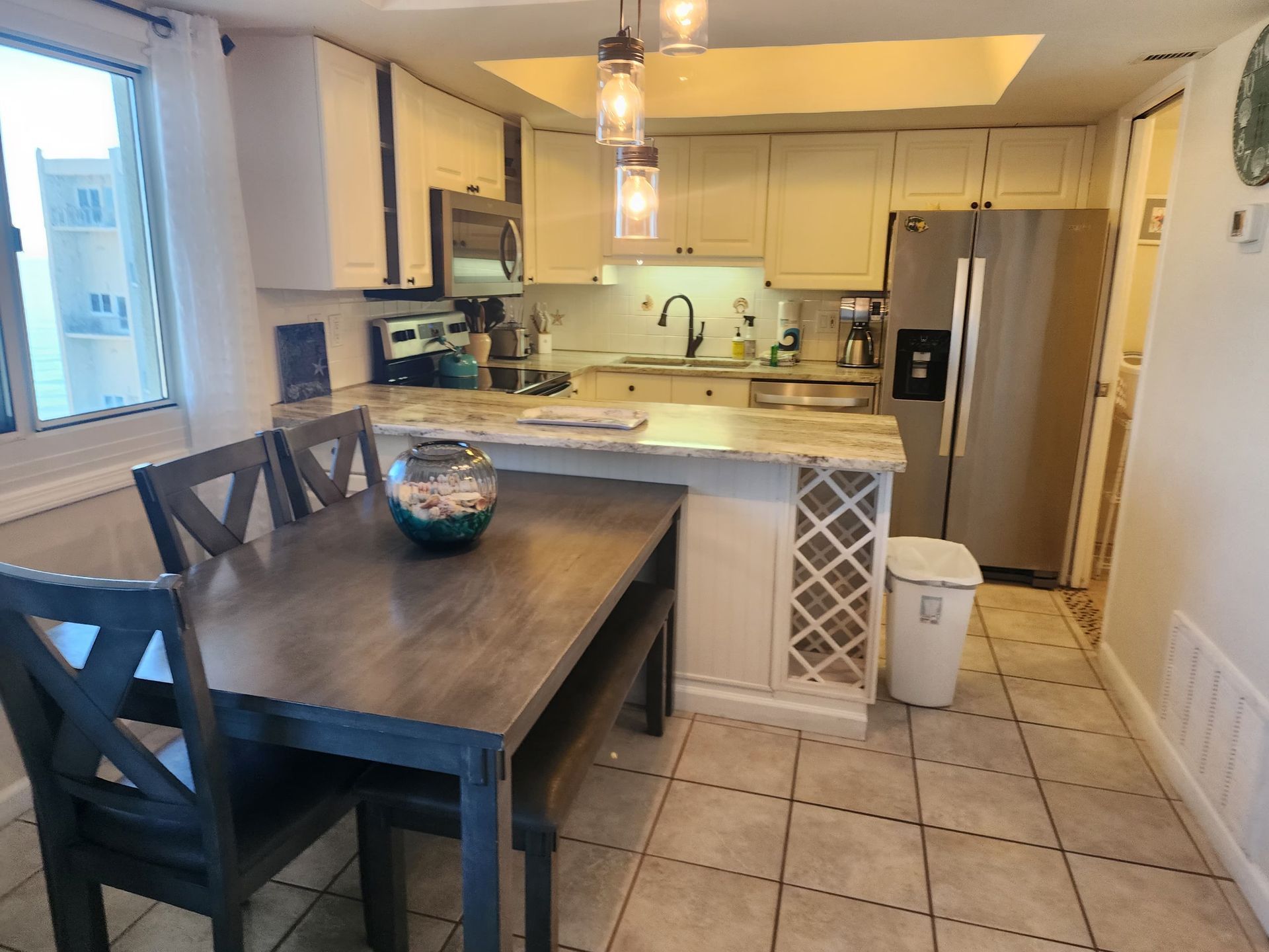 Kitchen with dining table, white cabinets, stainless steel refrigerator, and pendant lights.