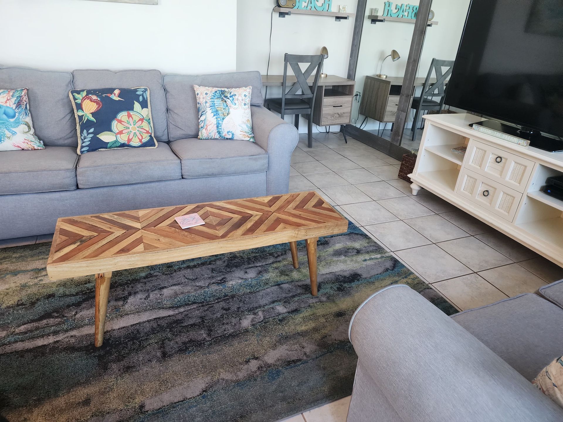 Living room with gray sofa, patterned rug, wooden coffee table, and TV on a white cabinet.