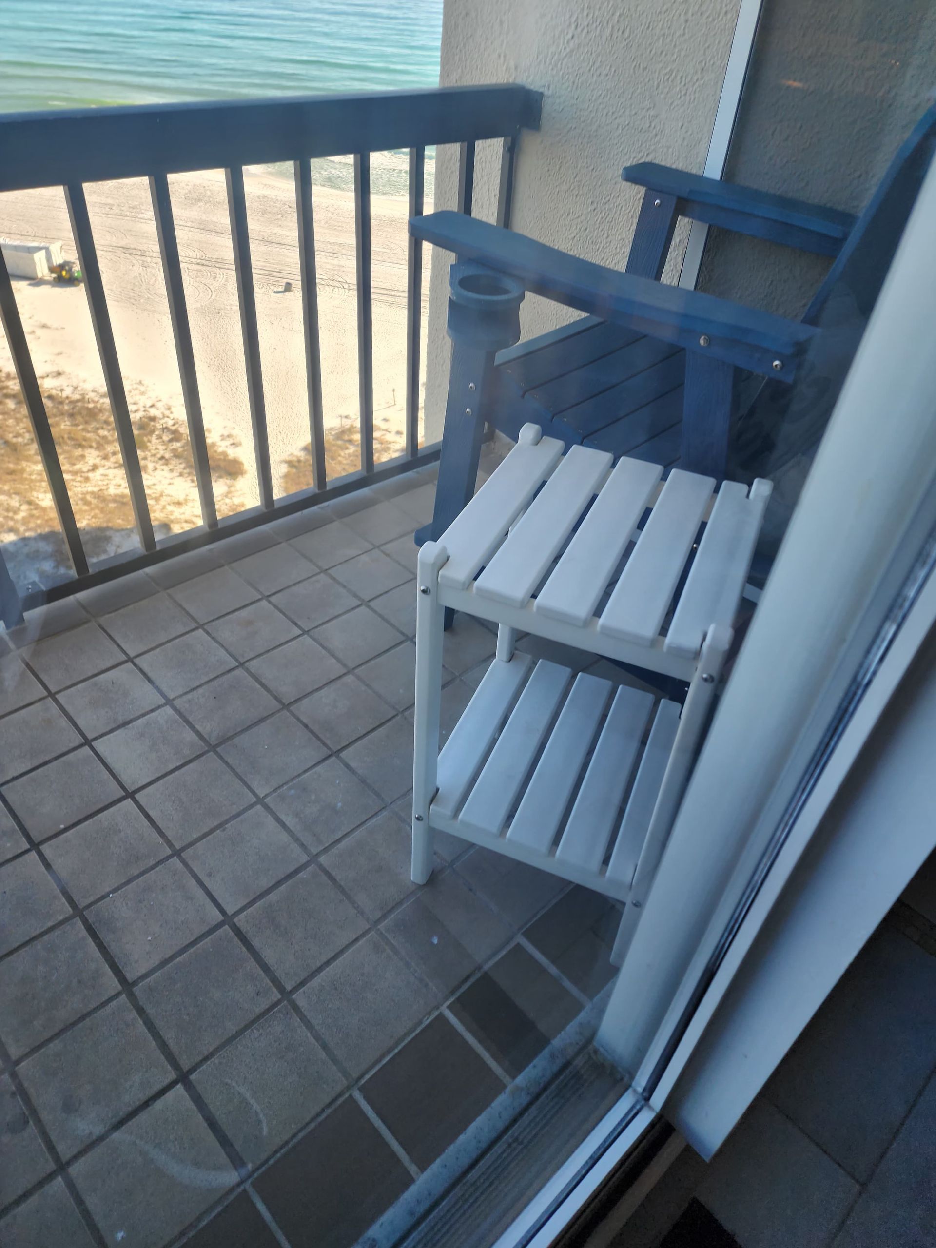 Balcony with blue chairs, small white table, beach view.