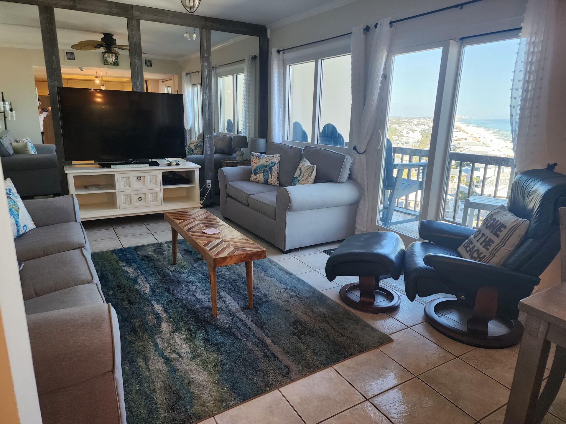 Living room with sectional sofa, TV, and ocean view from a balcony.