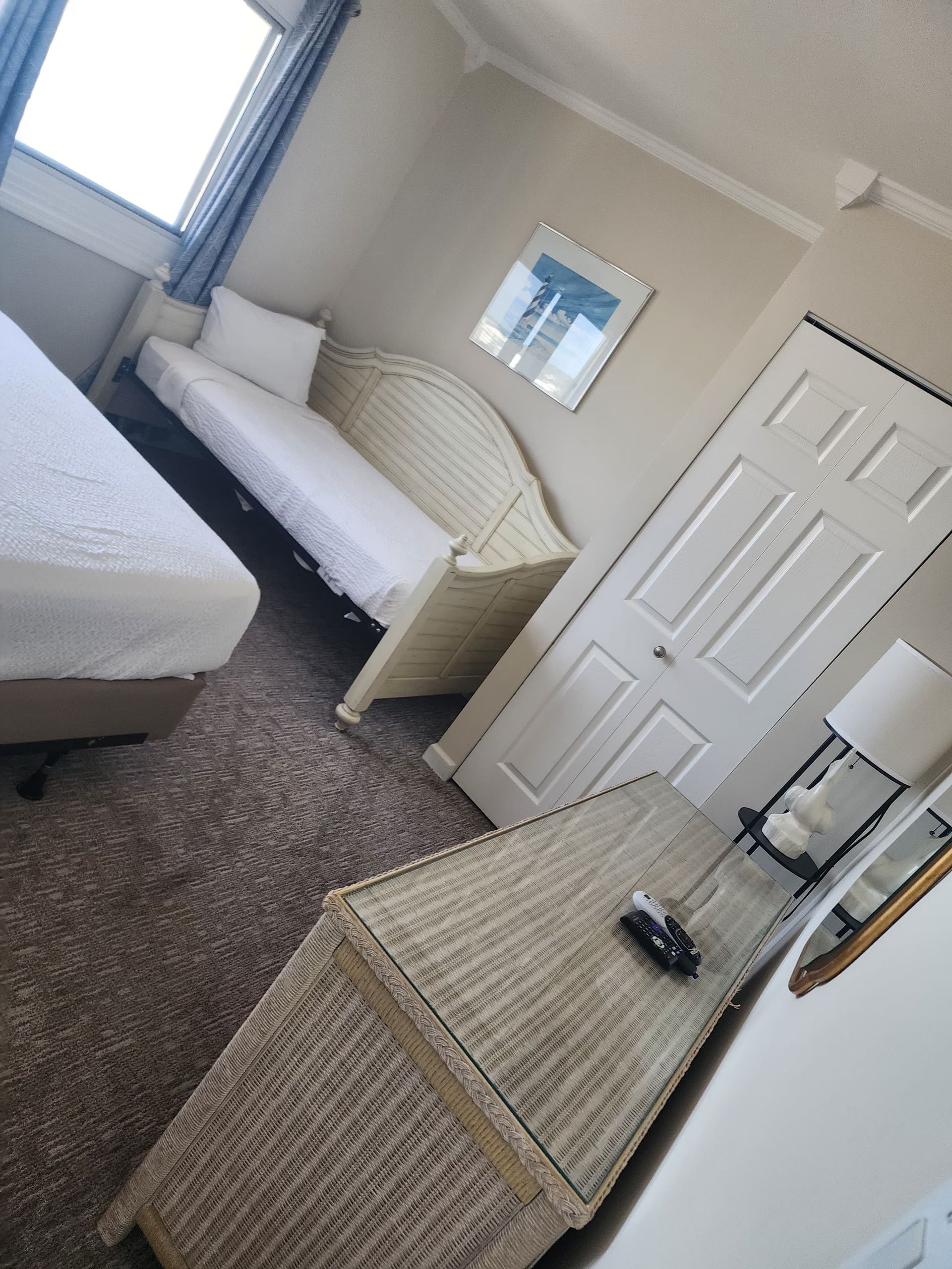 Bedroom with two beds, wicker furniture, and a closet. Beige walls, neutral carpet.
