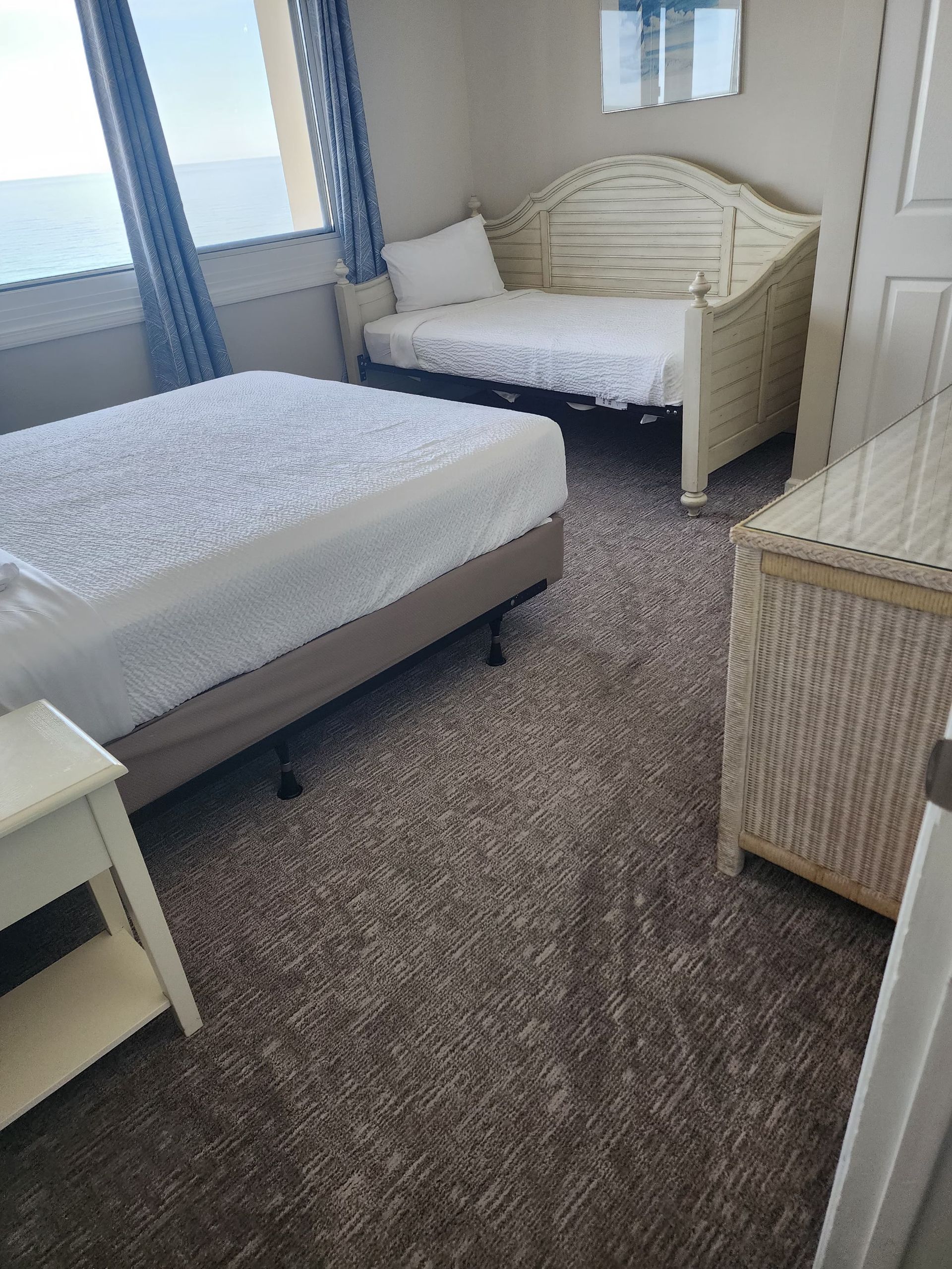 Bedroom with two beds, one daybed, and a white wicker chest on a brown carpet.