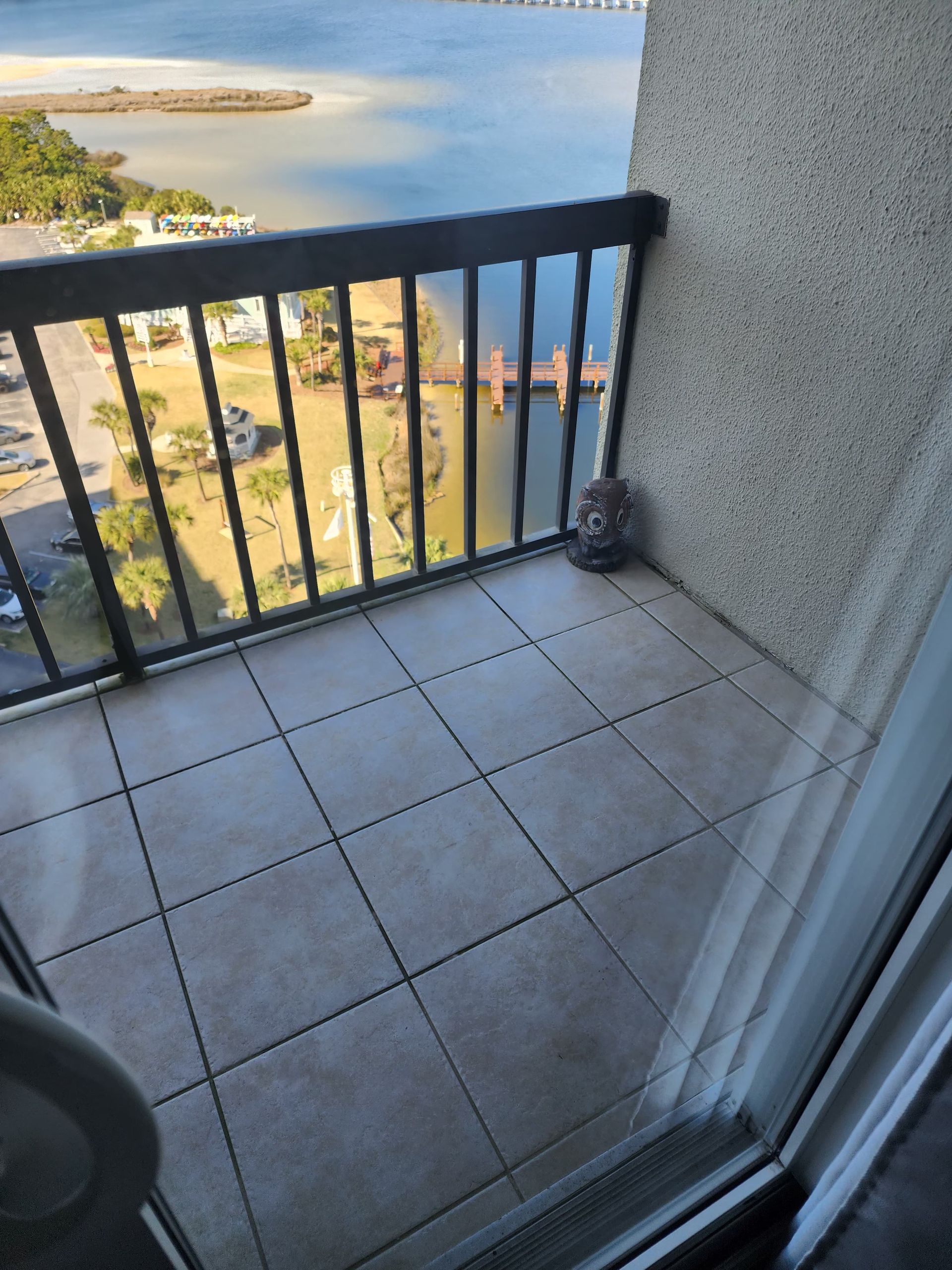 Balcony with tiled floor and black railing overlooking water and buildings.