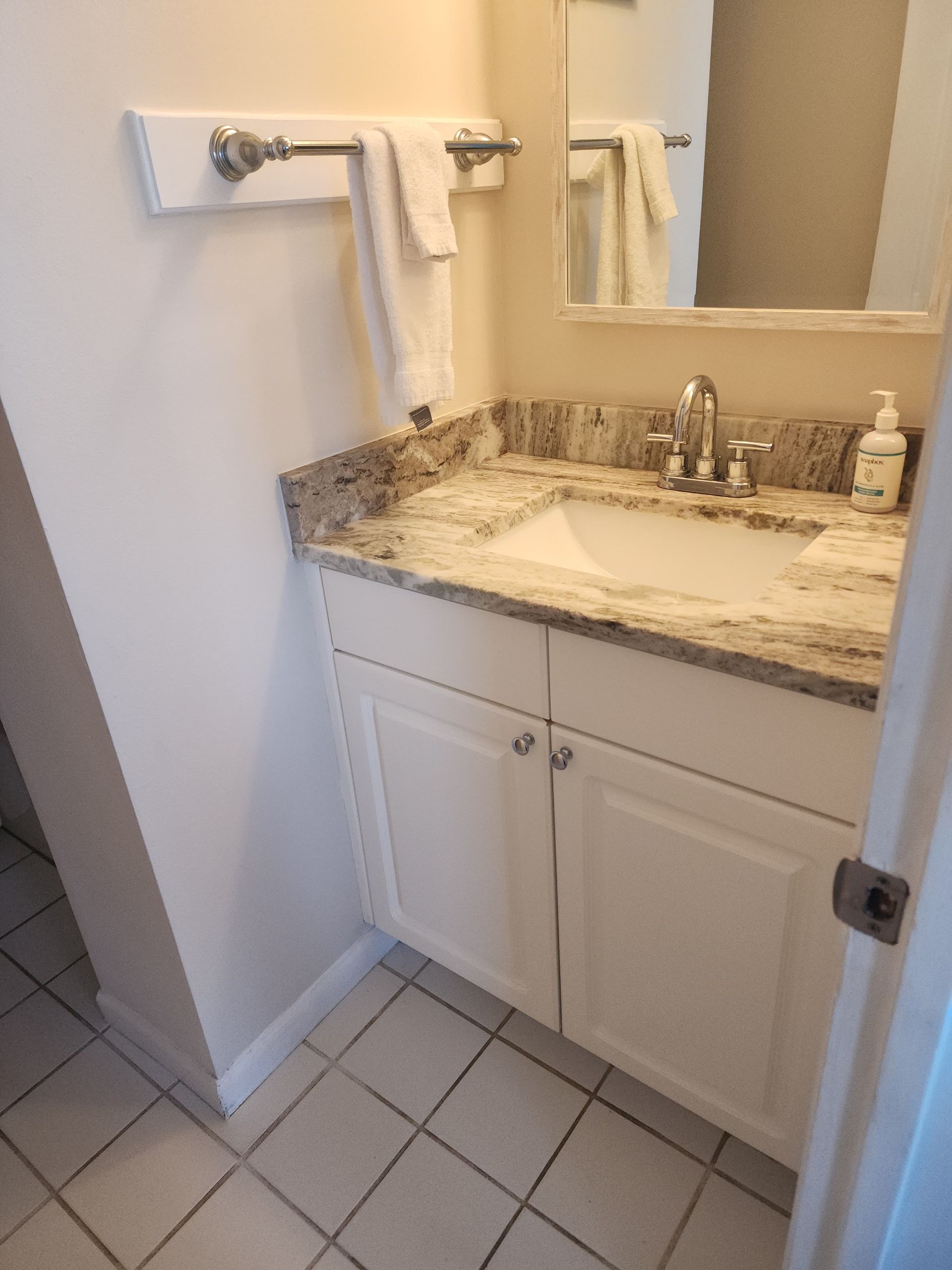 Bathroom with white cabinets, granite countertop, sink, mirror, towel bar, and white floor tiles.