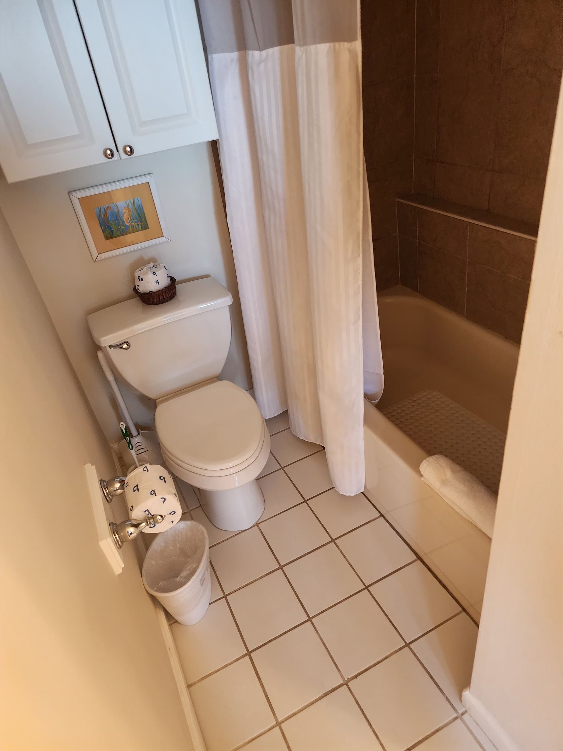 Small bathroom with toilet, bathtub, and white tile floor.