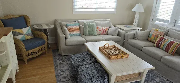 Living room with light-colored couches, wicker chair, white coffee table, and patterned pillows.