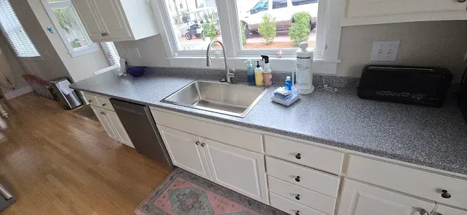 A kitchen with white cabinets, a stainless steel sink, and a black speckled countertop. A window is behind the sink.