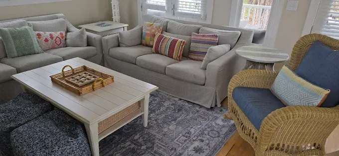 Cozy living room with light gray sofas, colorful pillows, wicker chair, and a white coffee table.